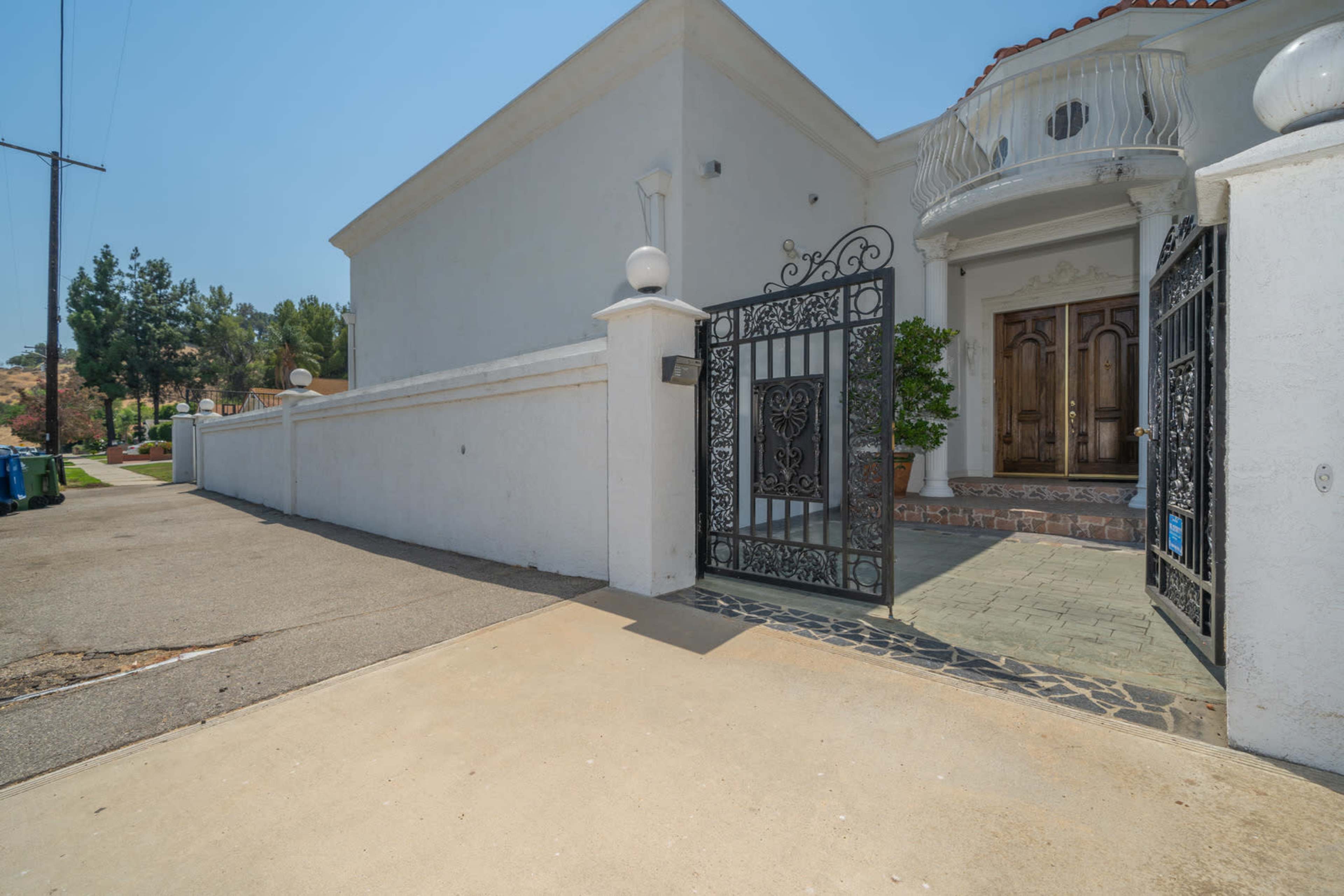 A wrought iron gate opens to a pathway leading to a residential entrance with double wooden doors.