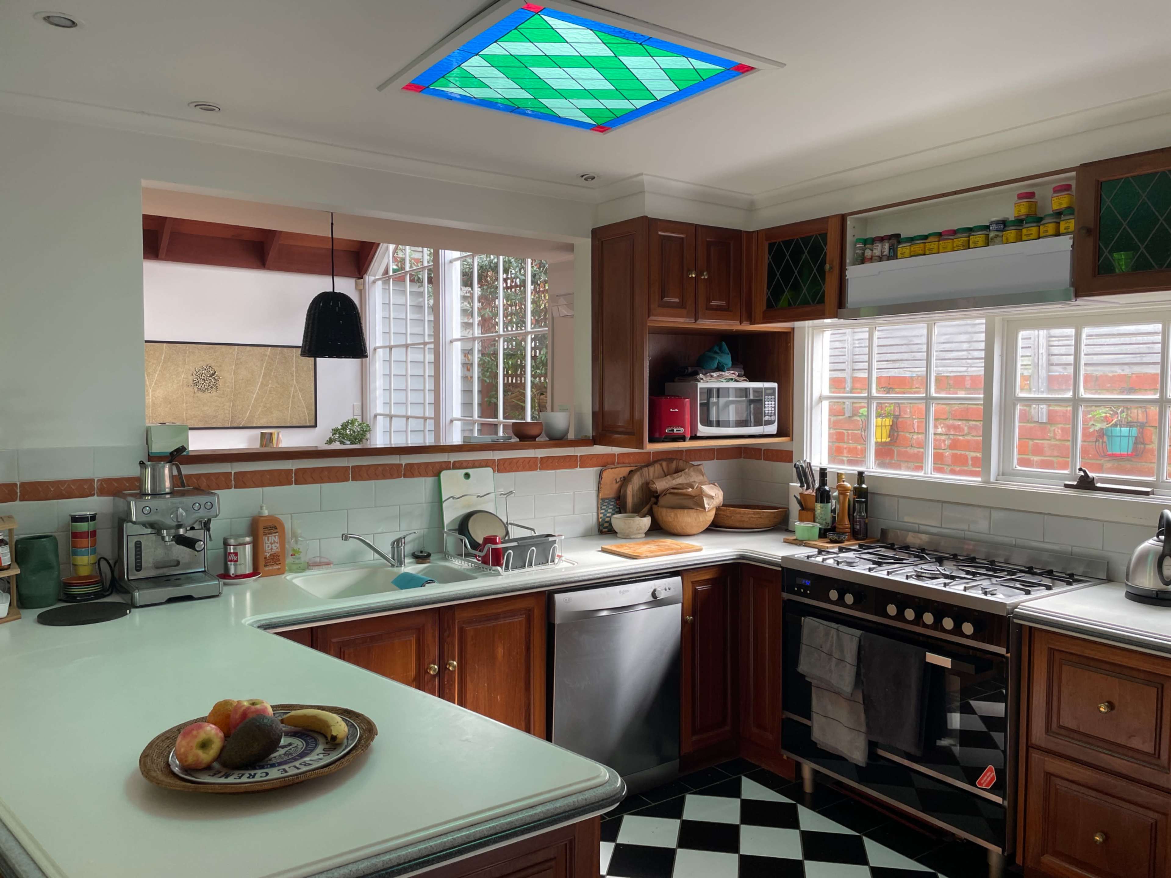A modern kitchen with wooden cabinets, a black and white checkered floor, and a skylight featuring a stained glass design.