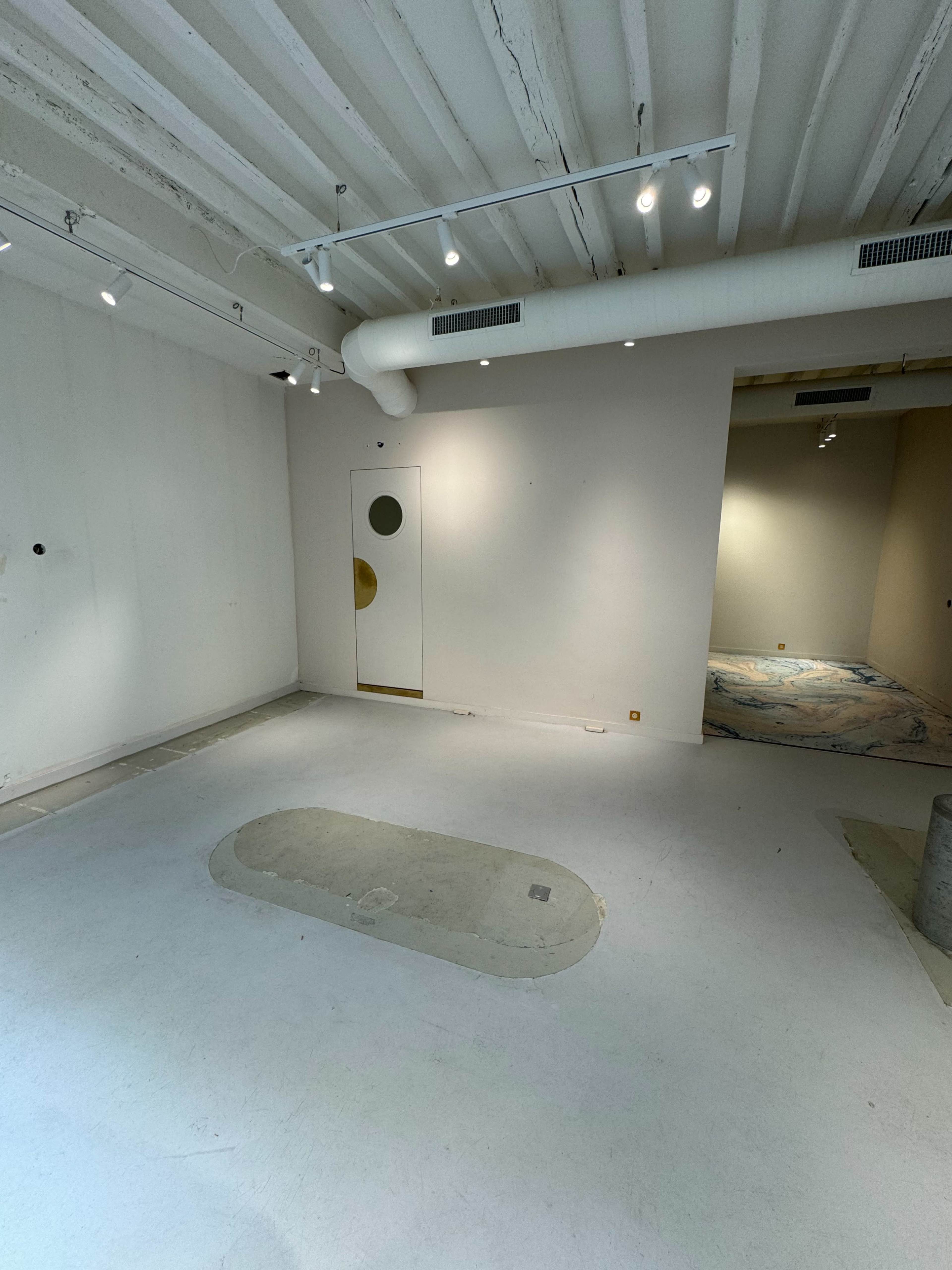 A spacious, empty room with white walls, a circular door on the left, and a partially visible area in the back.