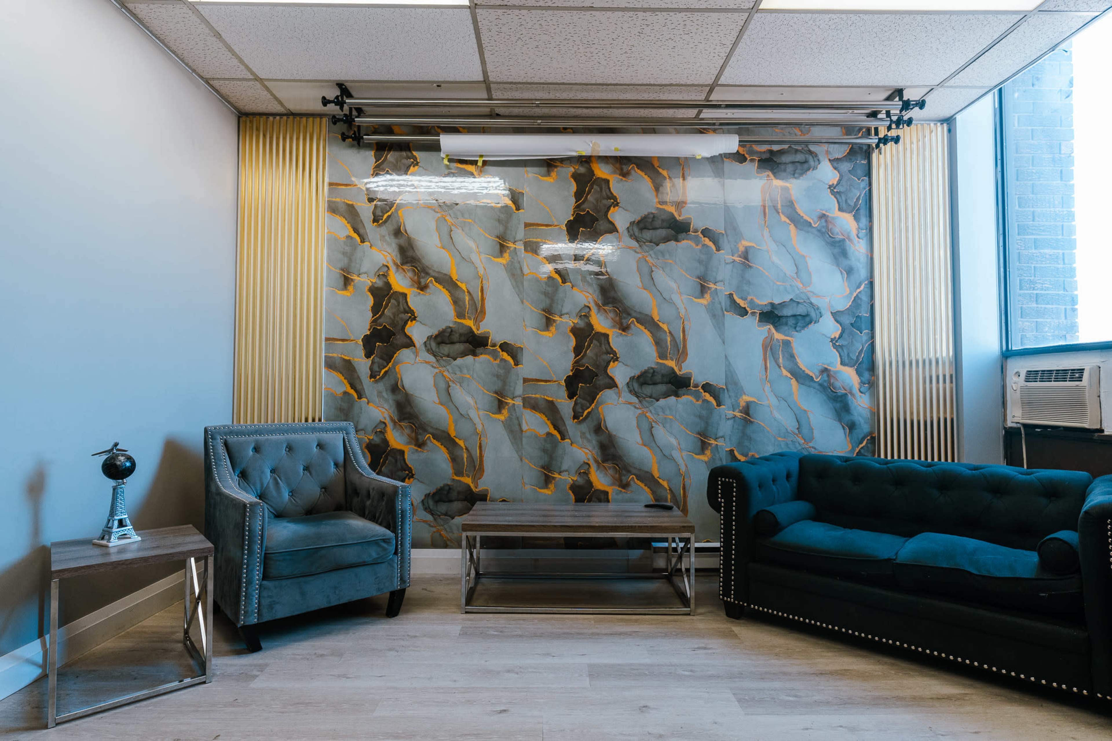 The image shows a stylish waiting area with two upholstered couches, a glass coffee table, and a decorative wall featuring an abstract pattern.