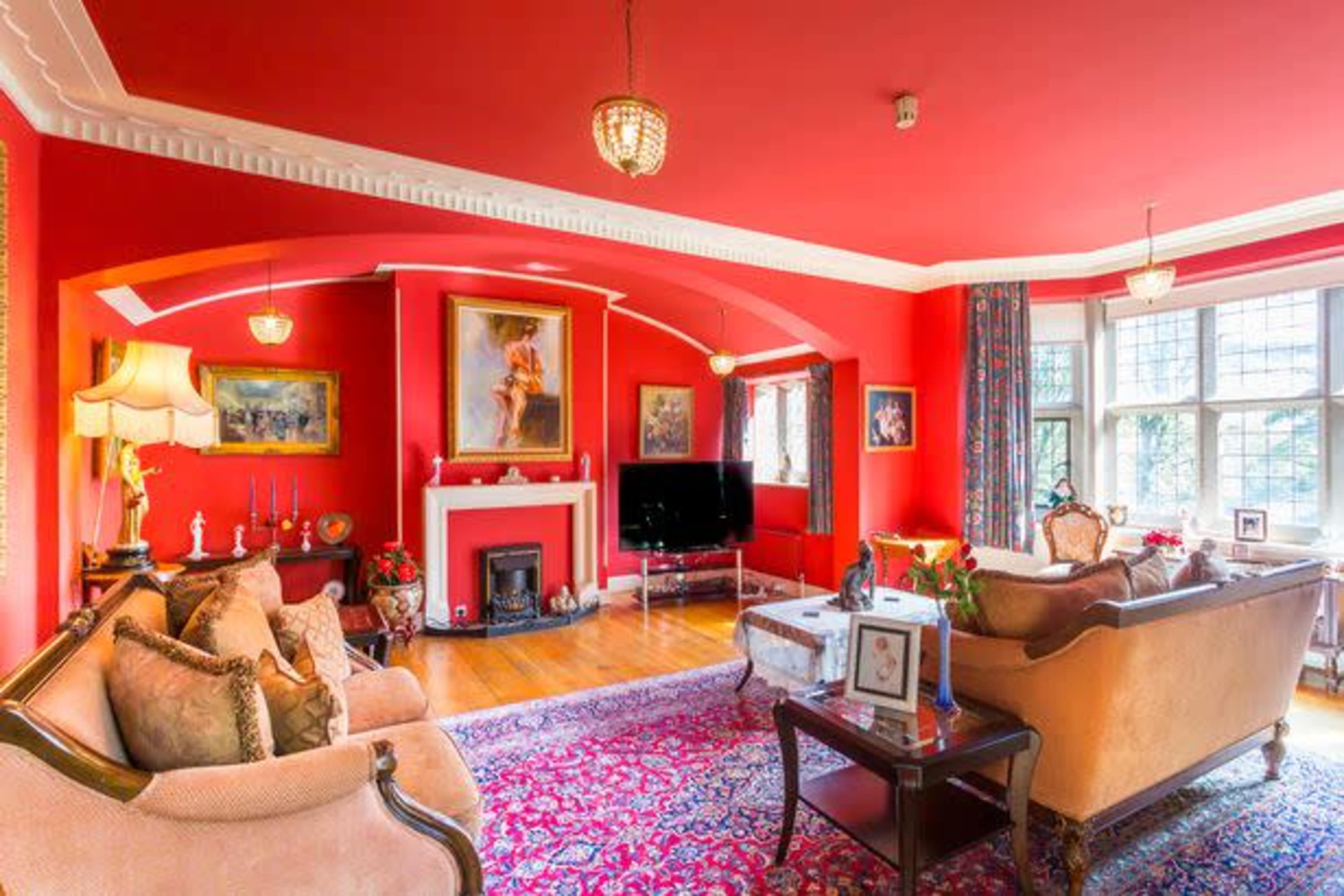 A living room with red walls features a large window, ornate furniture, a television, and decorative artwork.