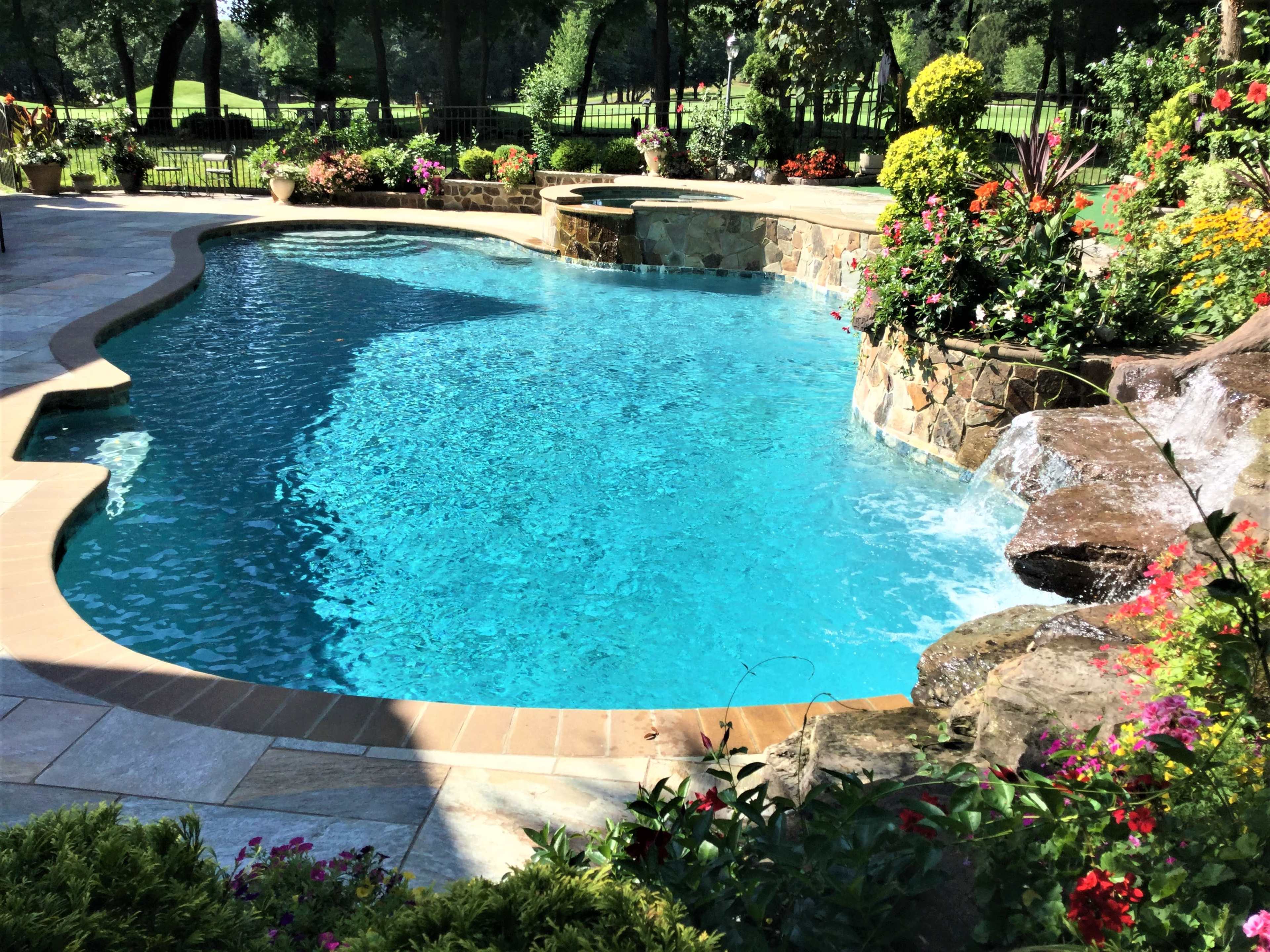 A clear blue swimming pool is surrounded by stone landscaping and vibrant flowers.