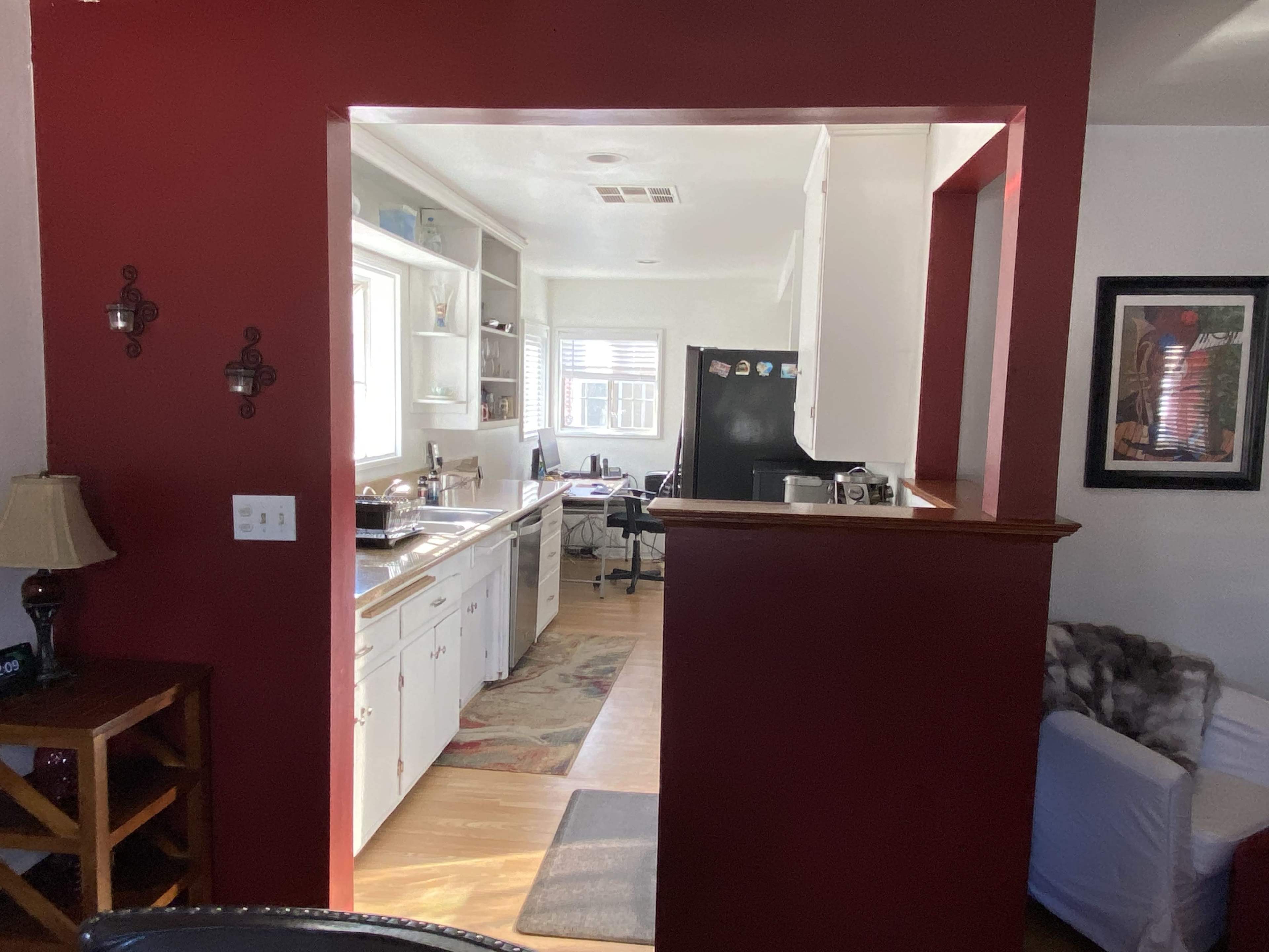 The image shows a kitchen with white cabinets and a black refrigerator, visible through an opening in a wall painted red.