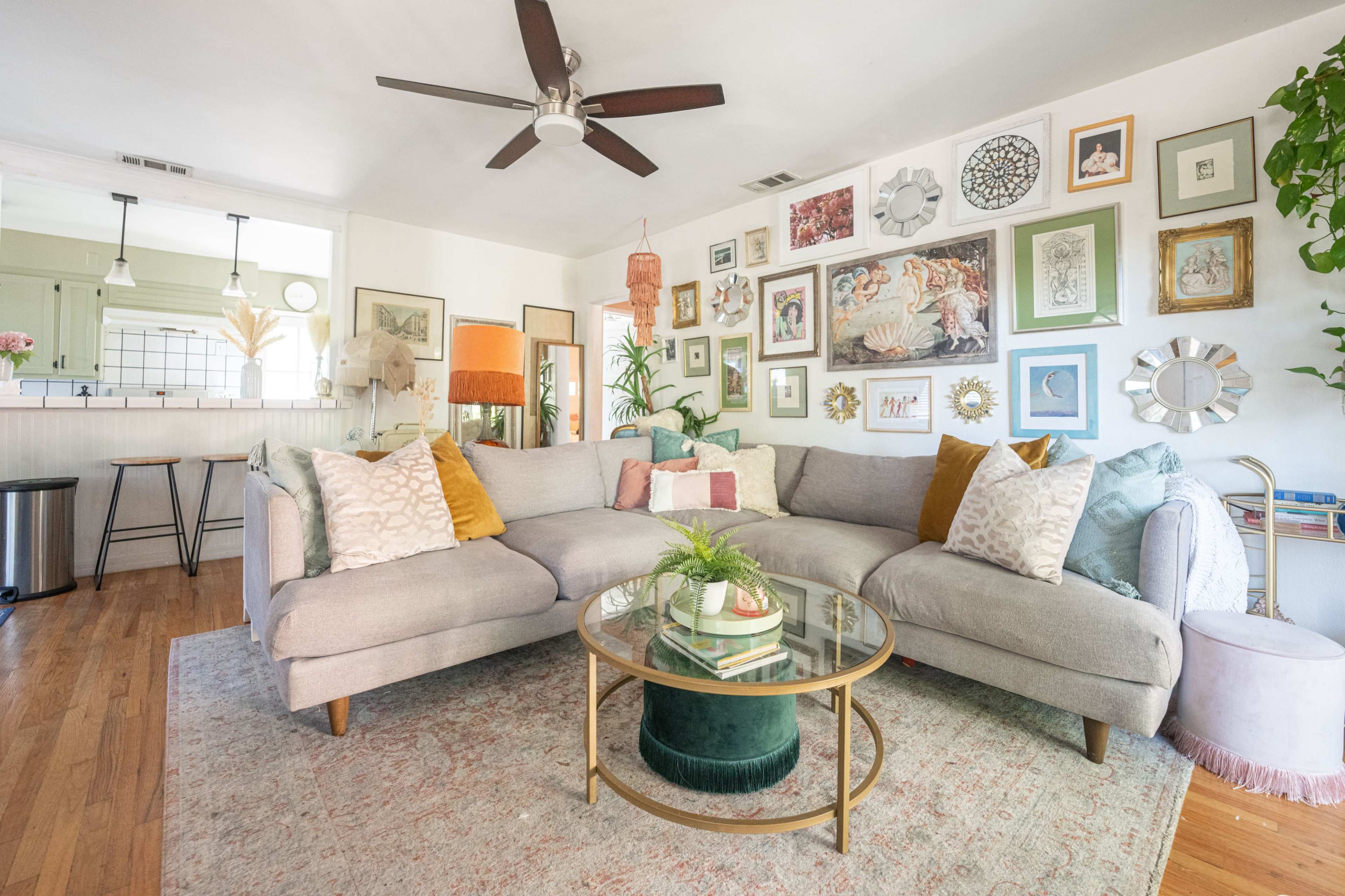 The image shows a modern living room with a large gray sectional sofa, a glass coffee table, and various framed artworks arranged on the wall.