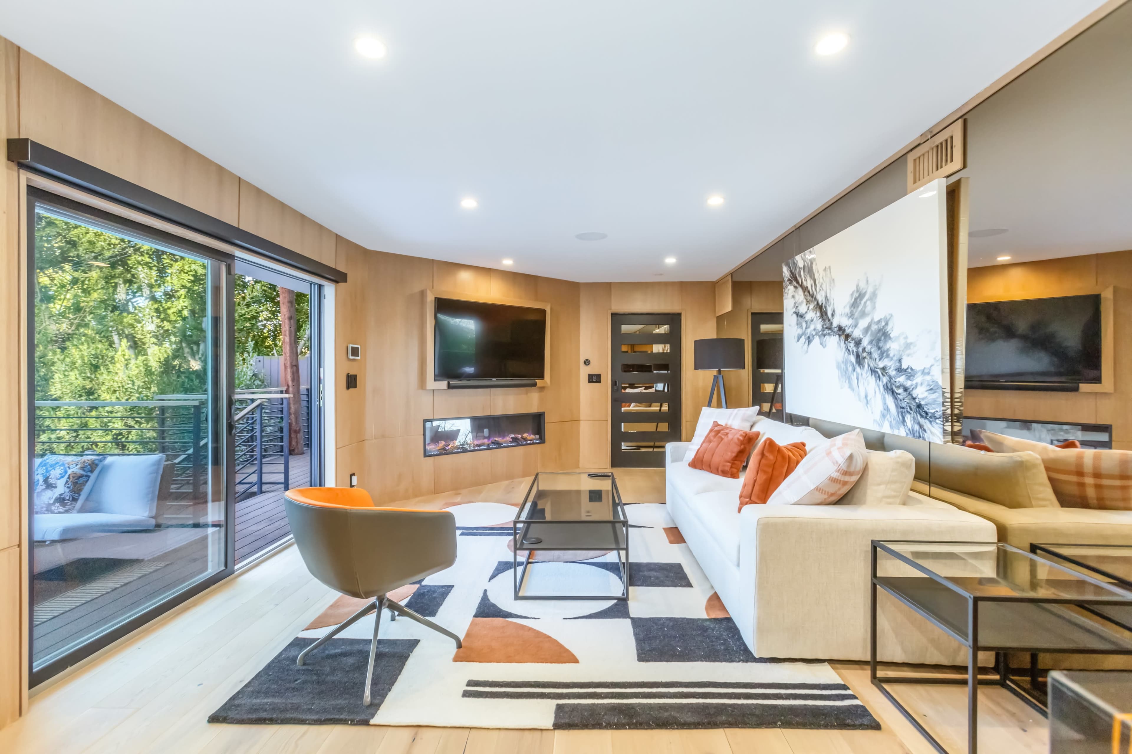A modern living room features a white sectional sofa, a glass coffee table on a patterned rug, and large windows that open to a balcony.