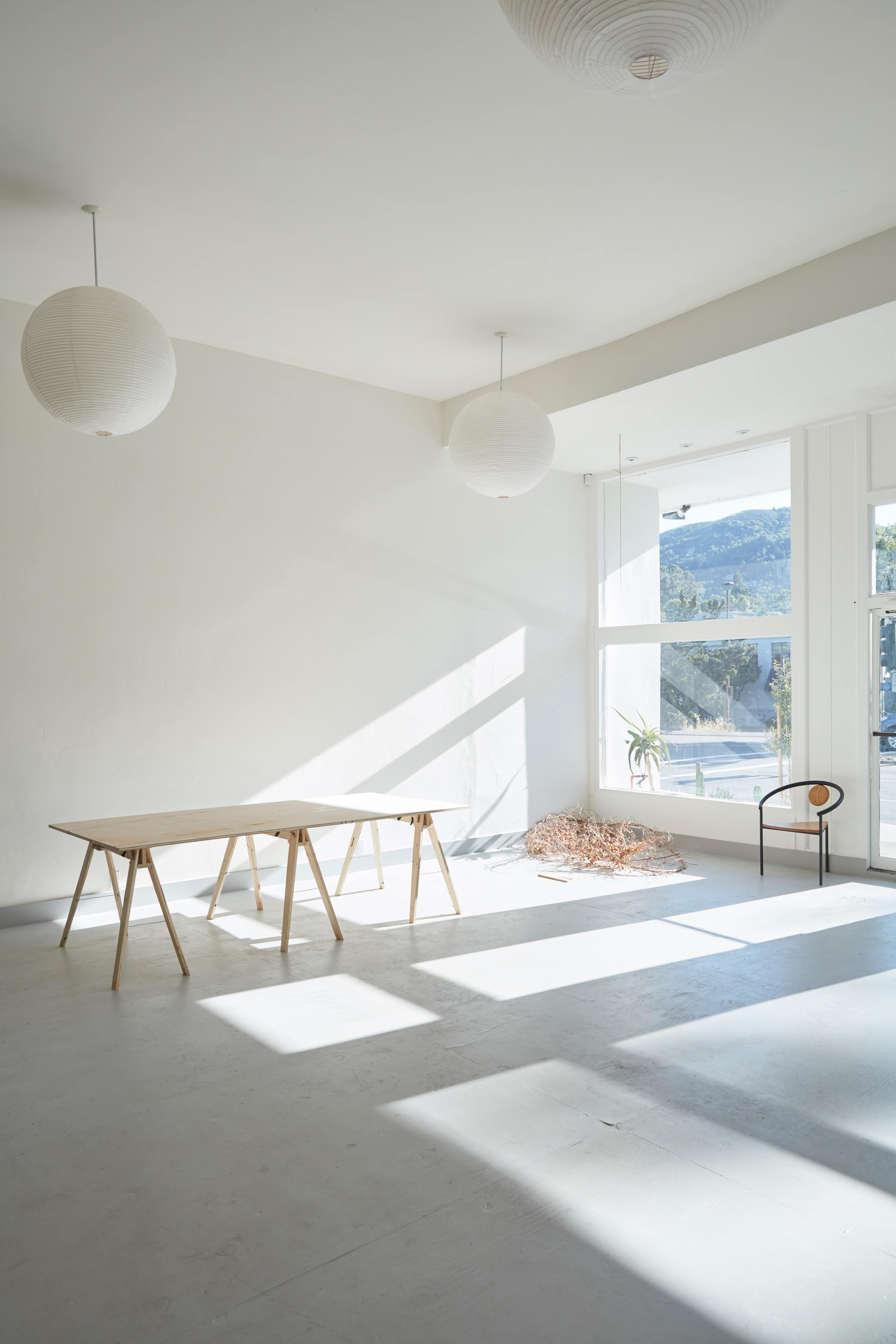 A bright room features a wooden table, a chair, and natural light streaming through large windows.