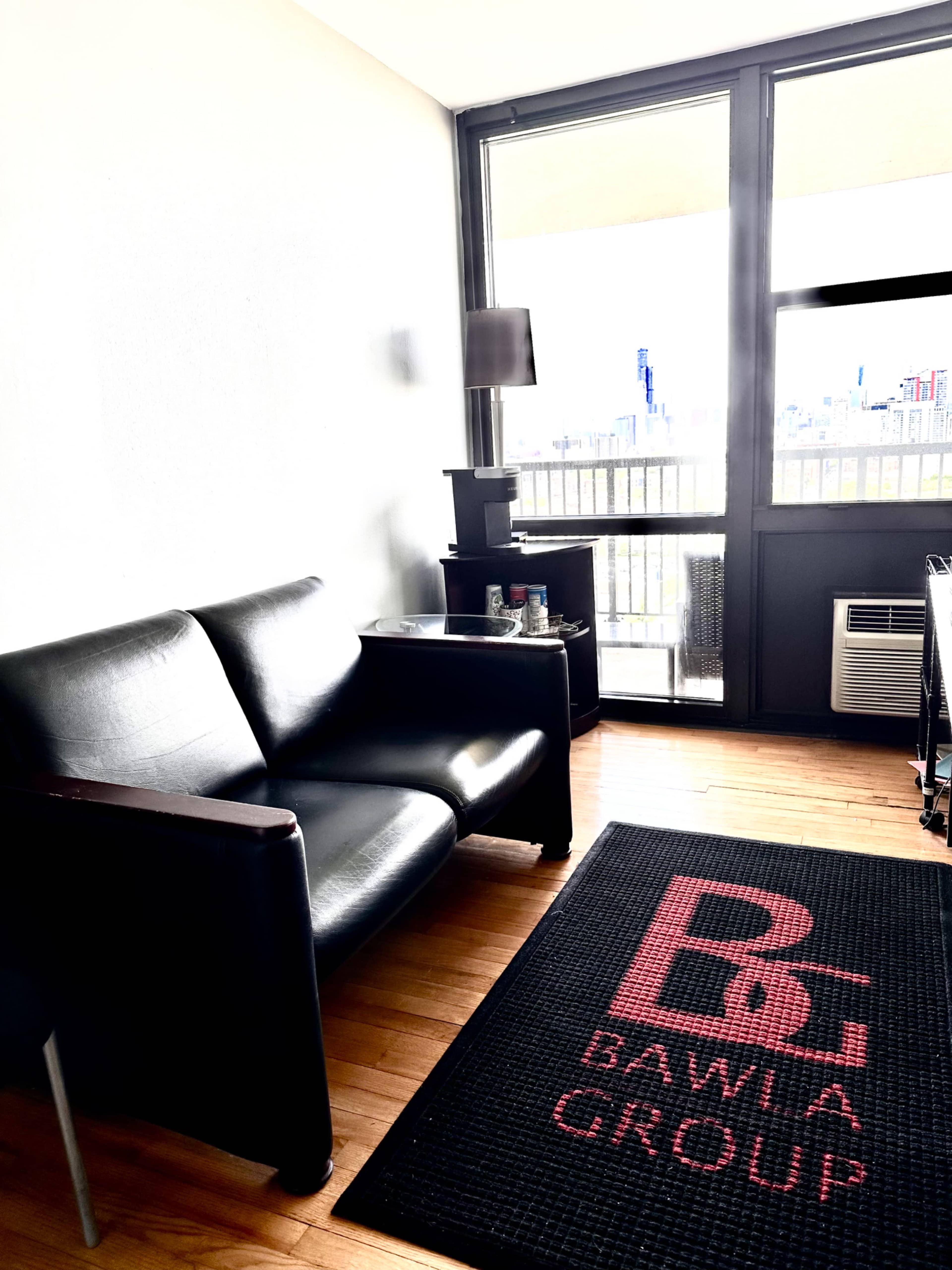 A black leather sofa sits beside a small black table in a well-lit room with a view of the city.