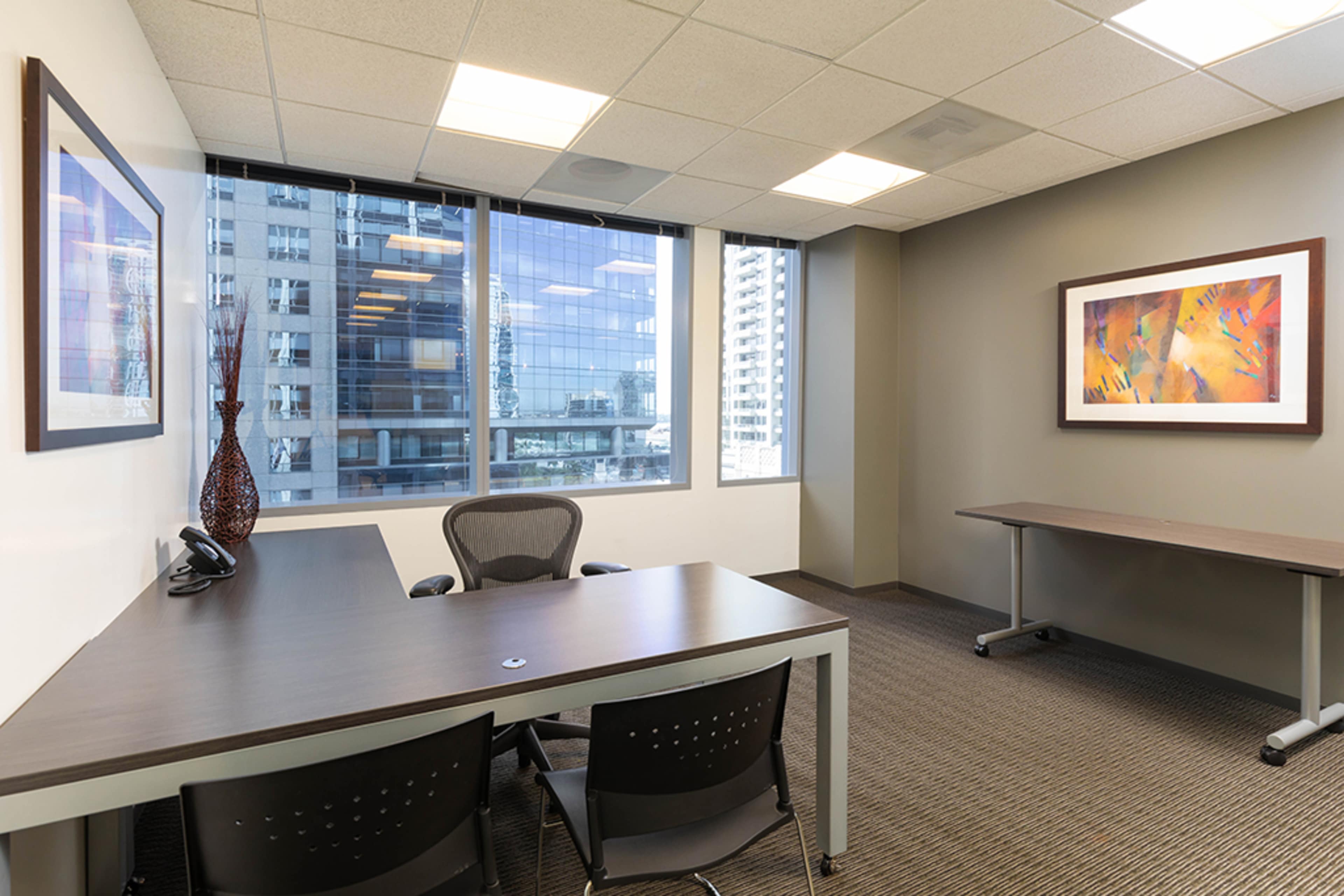 A sleek office space with a large desk, two chairs, and large windows overlooking a cityscape.