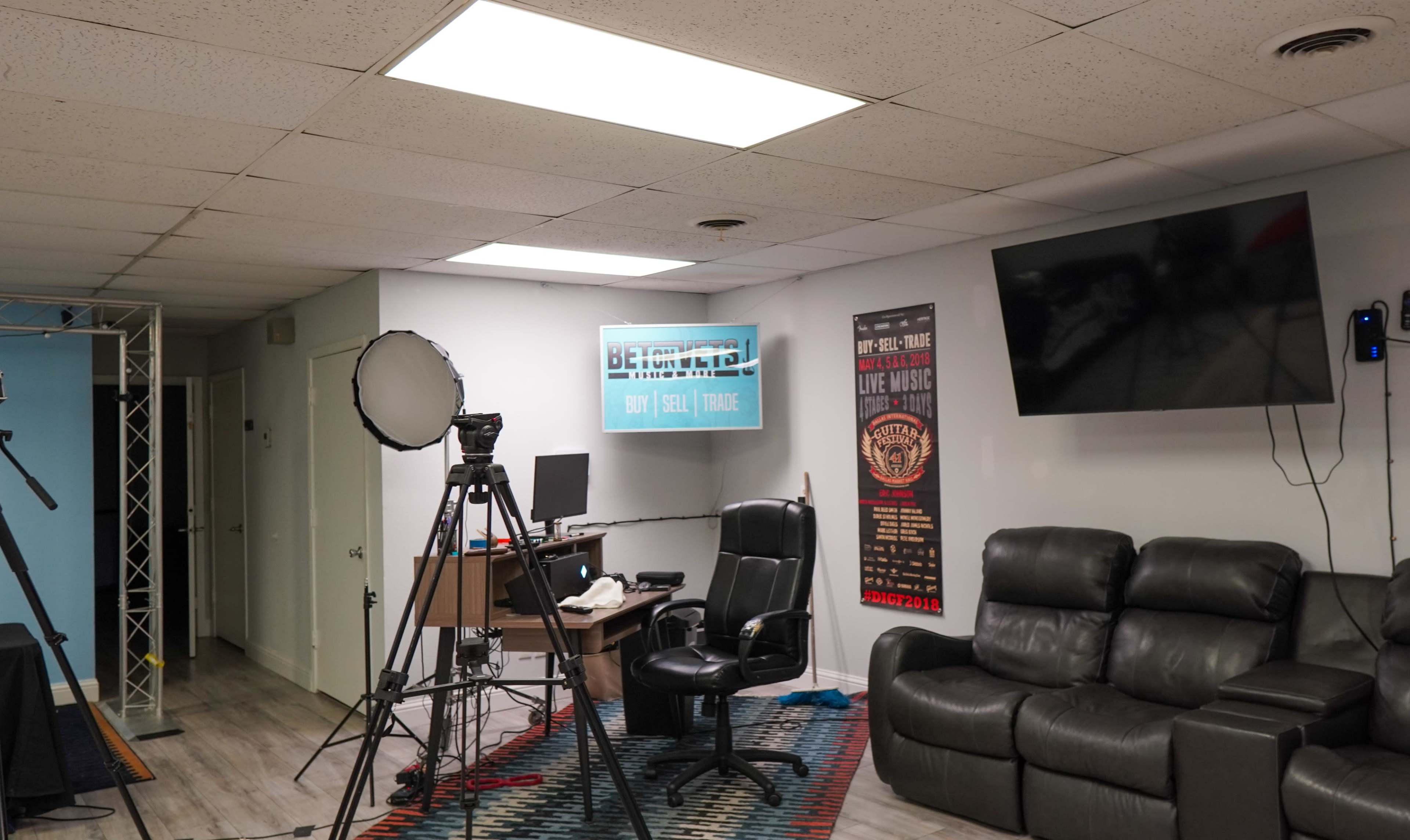 An office space with a camera on a tripod, a desk chair, and a large TV mounted on the wall.