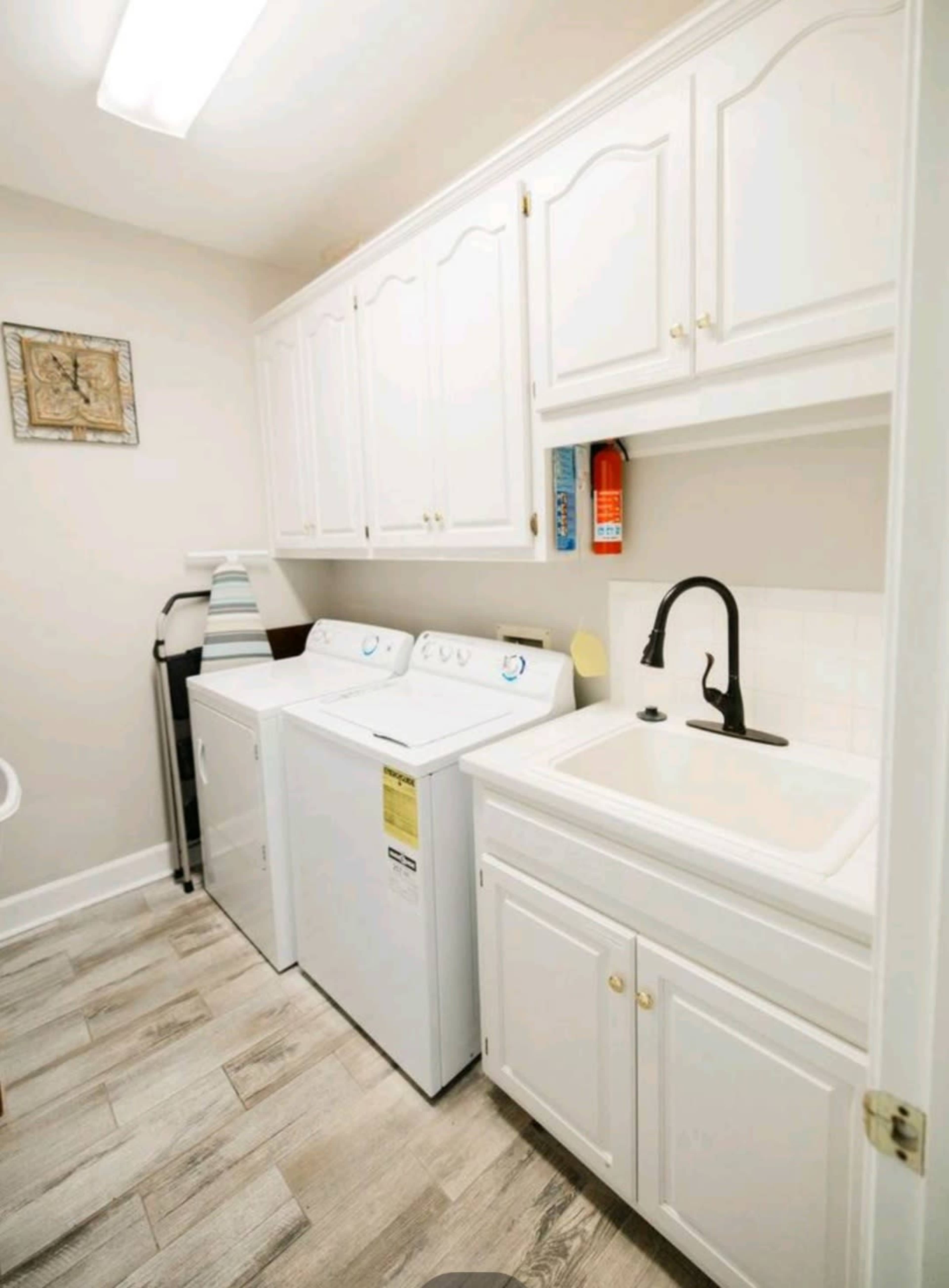 The image shows a laundry room with white cabinetry, a washing machine, a dryer, and a sink.