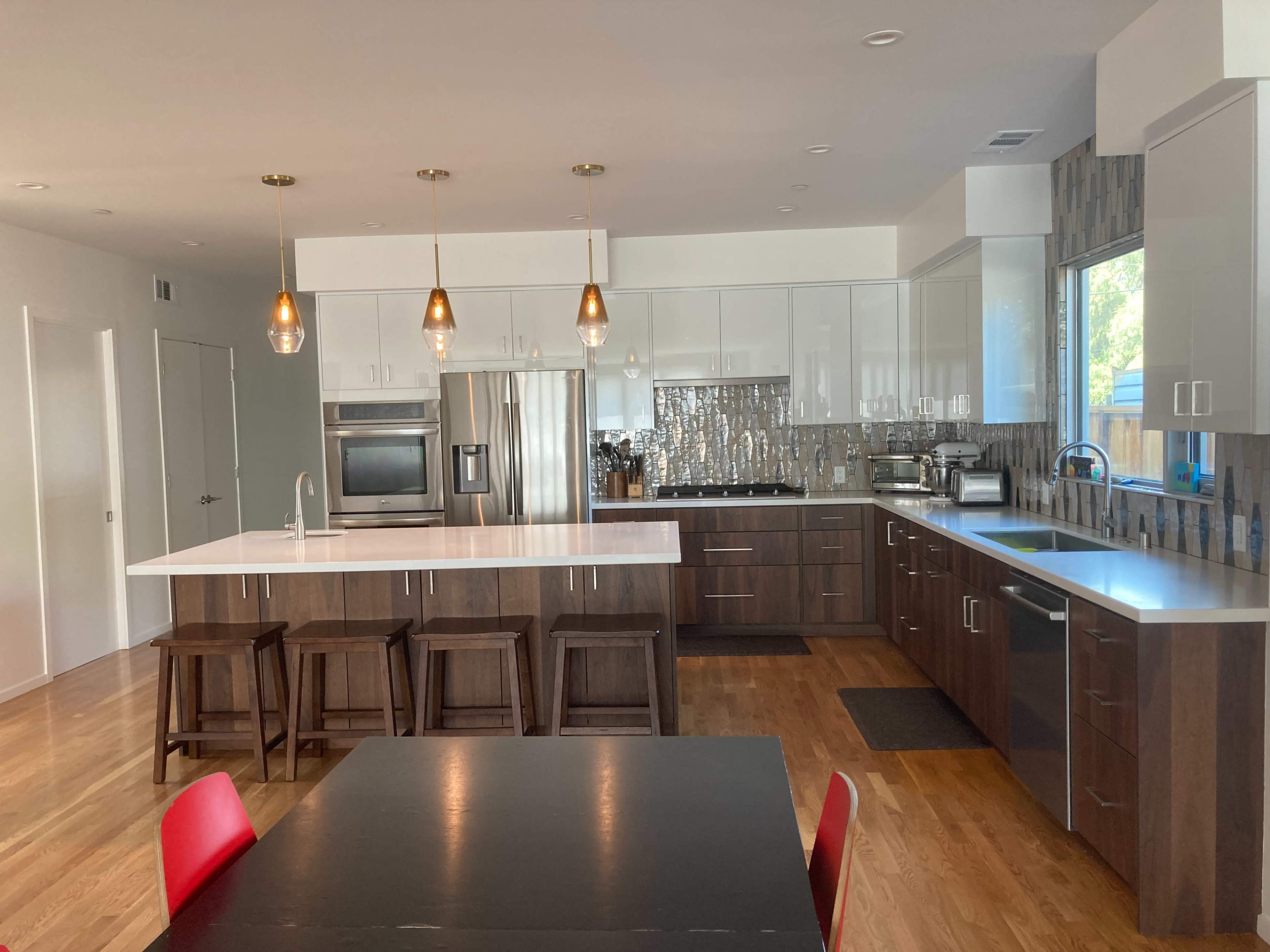 A modern kitchen features two-tone cabinetry, stainless steel appliances, pendant lighting, and a central island with seating.
