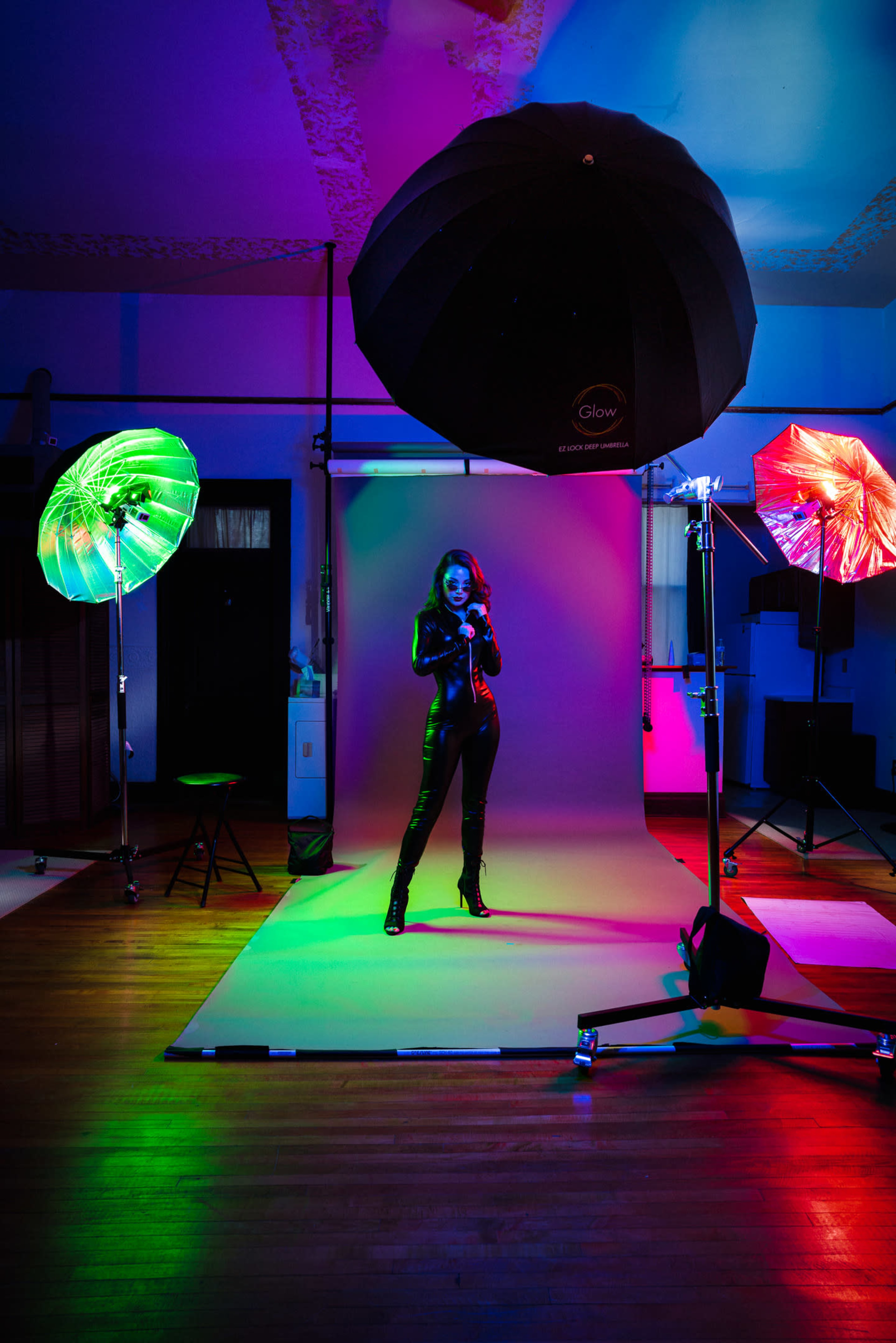 A model poses in a studio with colorful lighting from umbrellas and a backdrop.