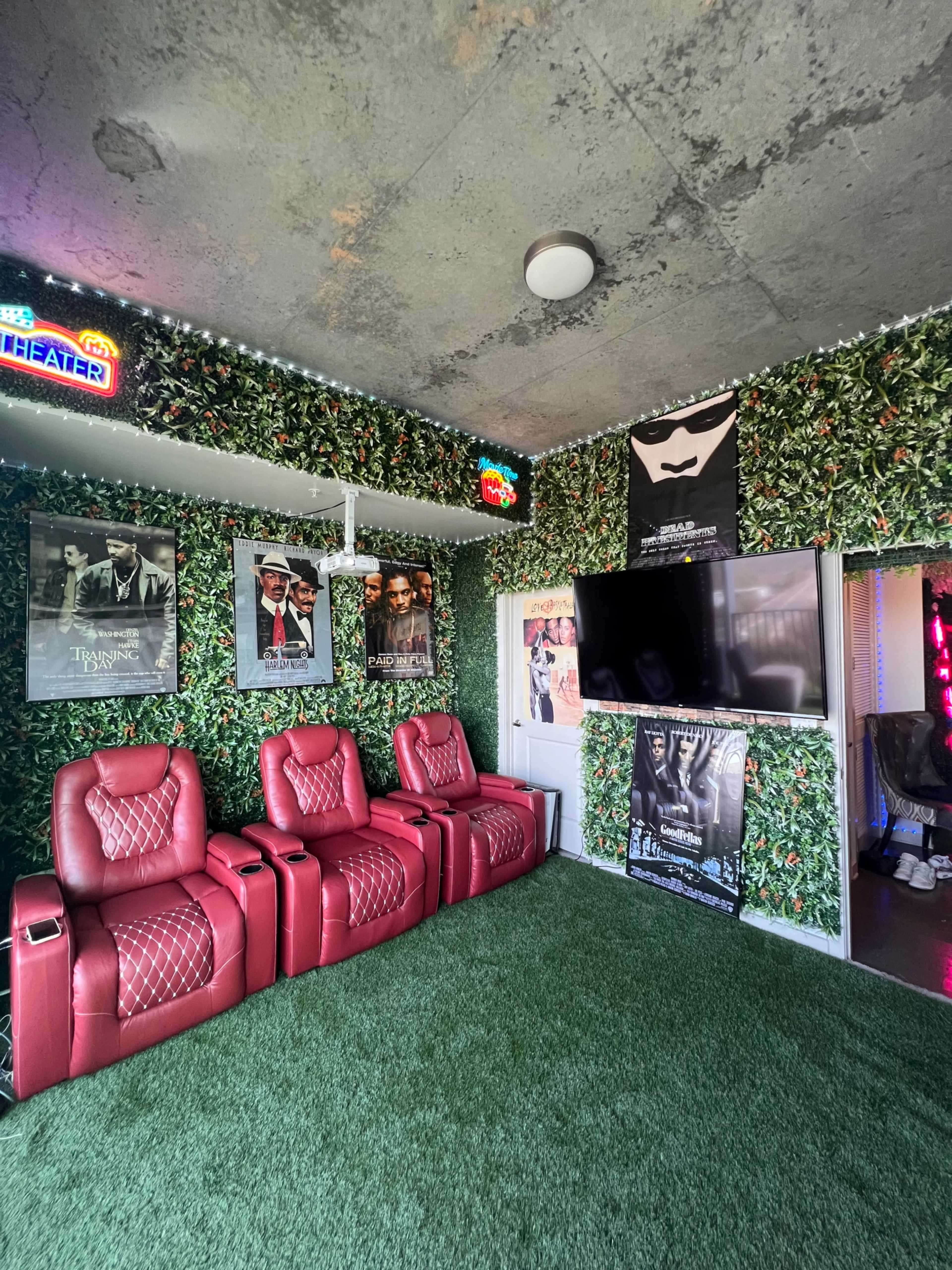 The image shows a home theater room with red reclining chairs, a large TV mounted on a wall, and walls decorated with leafy wallpaper and movie posters.