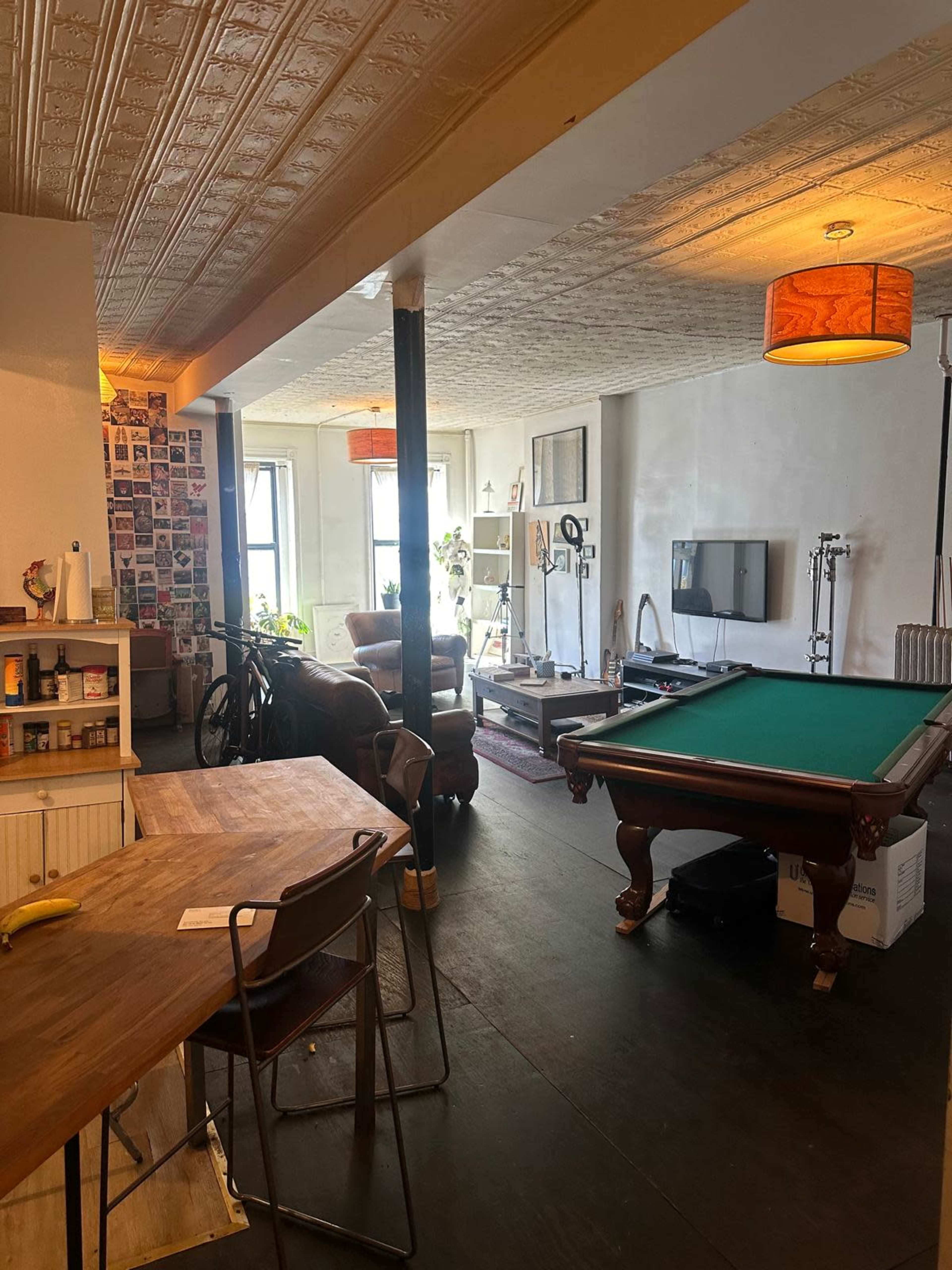 The image shows a spacious living area with a pool table, a dining table, and a lounge area furnished with a couch and entertainment equipment.