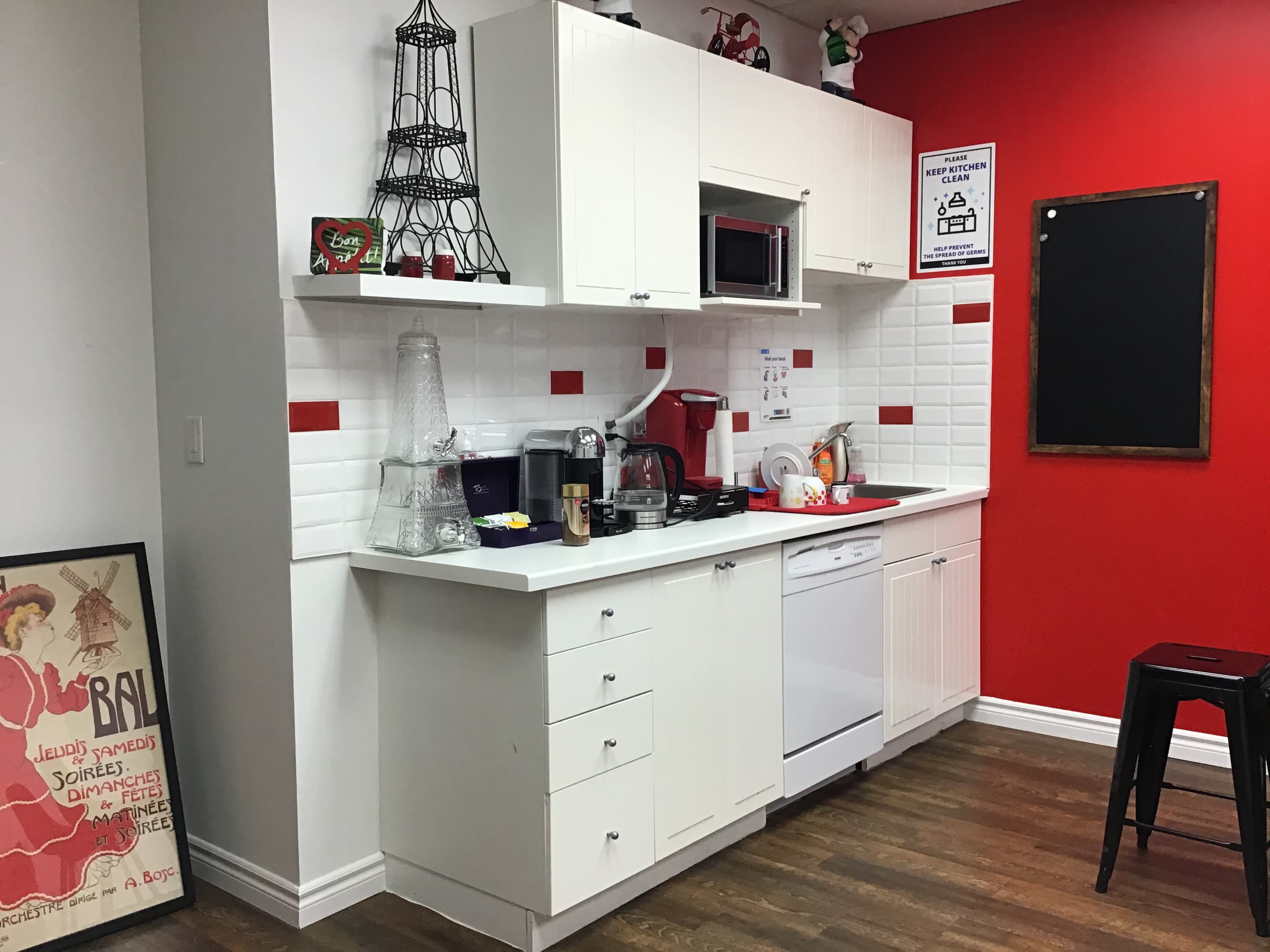A compact kitchen with white cabinetry, a microwave, and various kitchen appliances against a red accent wall.
