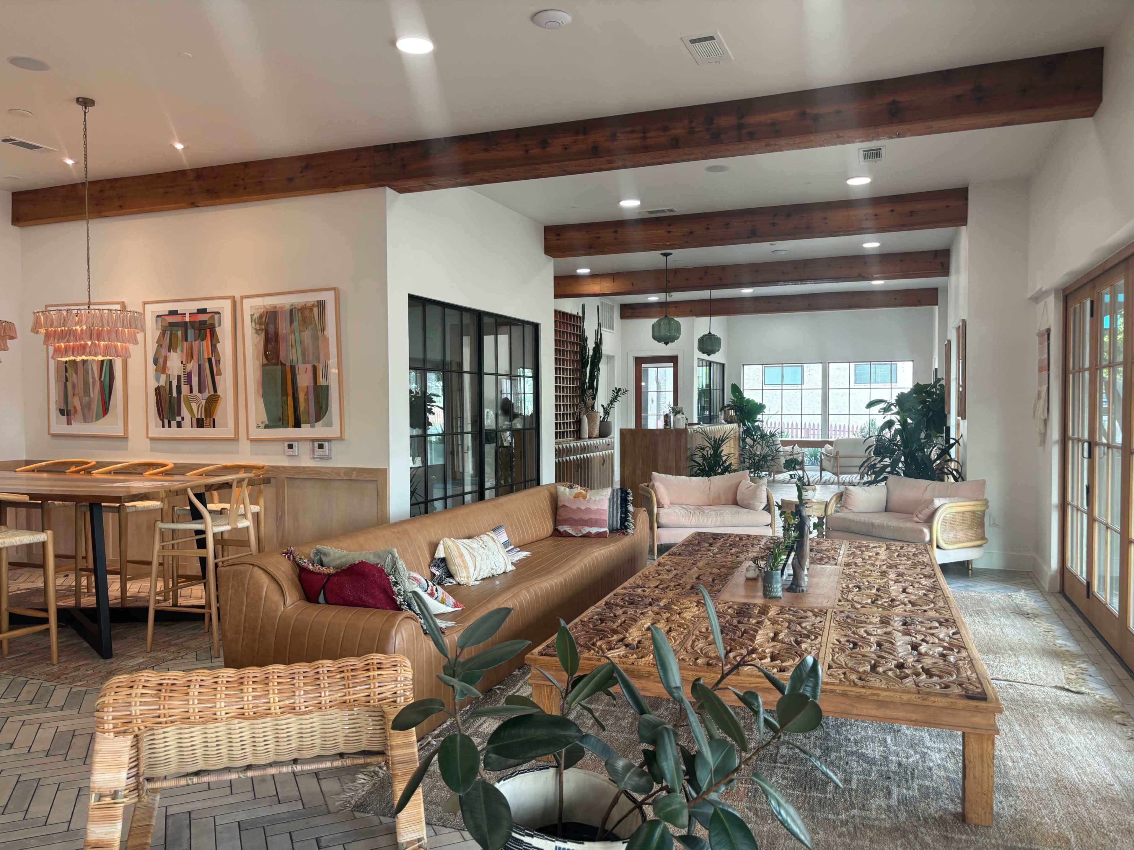 A modern living area with a large wooden coffee table, a brown leather sofa, dining area, and plants throughout the space.