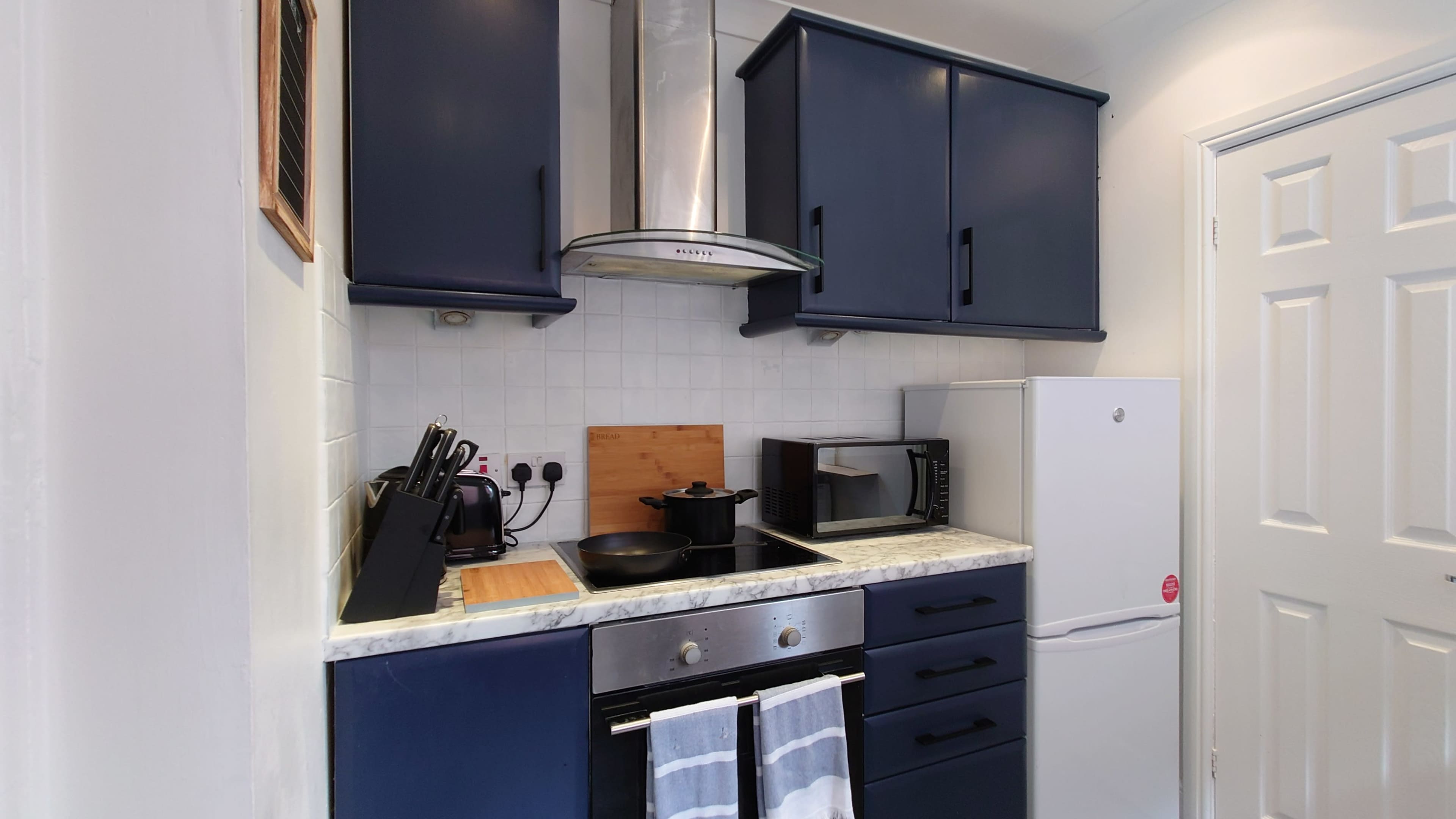 A compact kitchen with dark blue cabinets, a silver oven, a microwave, and a white refrigerator.