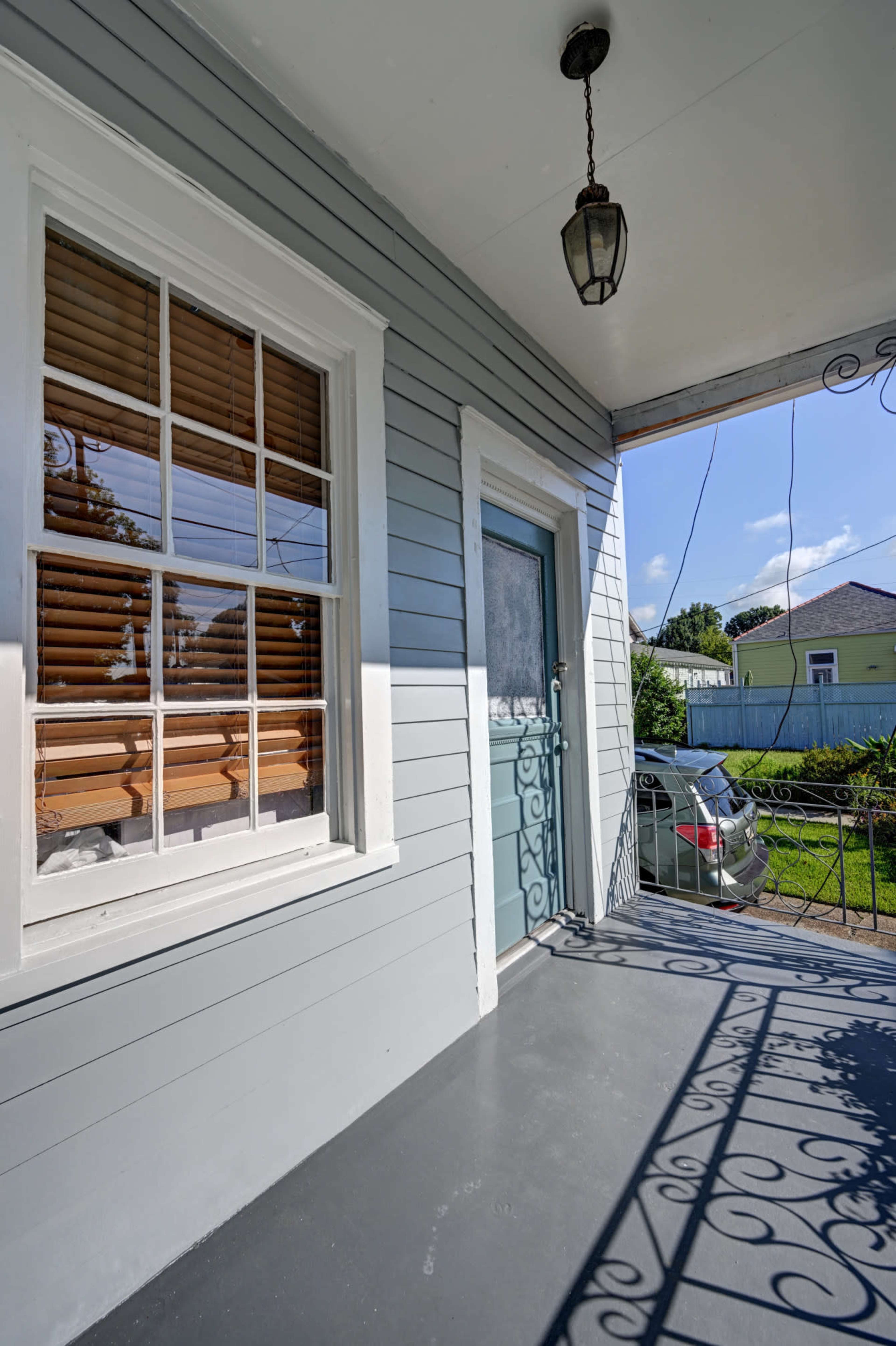 A porch with a light blue door and a window beside it, featuring wooden blinds, while a car is visible in the background.