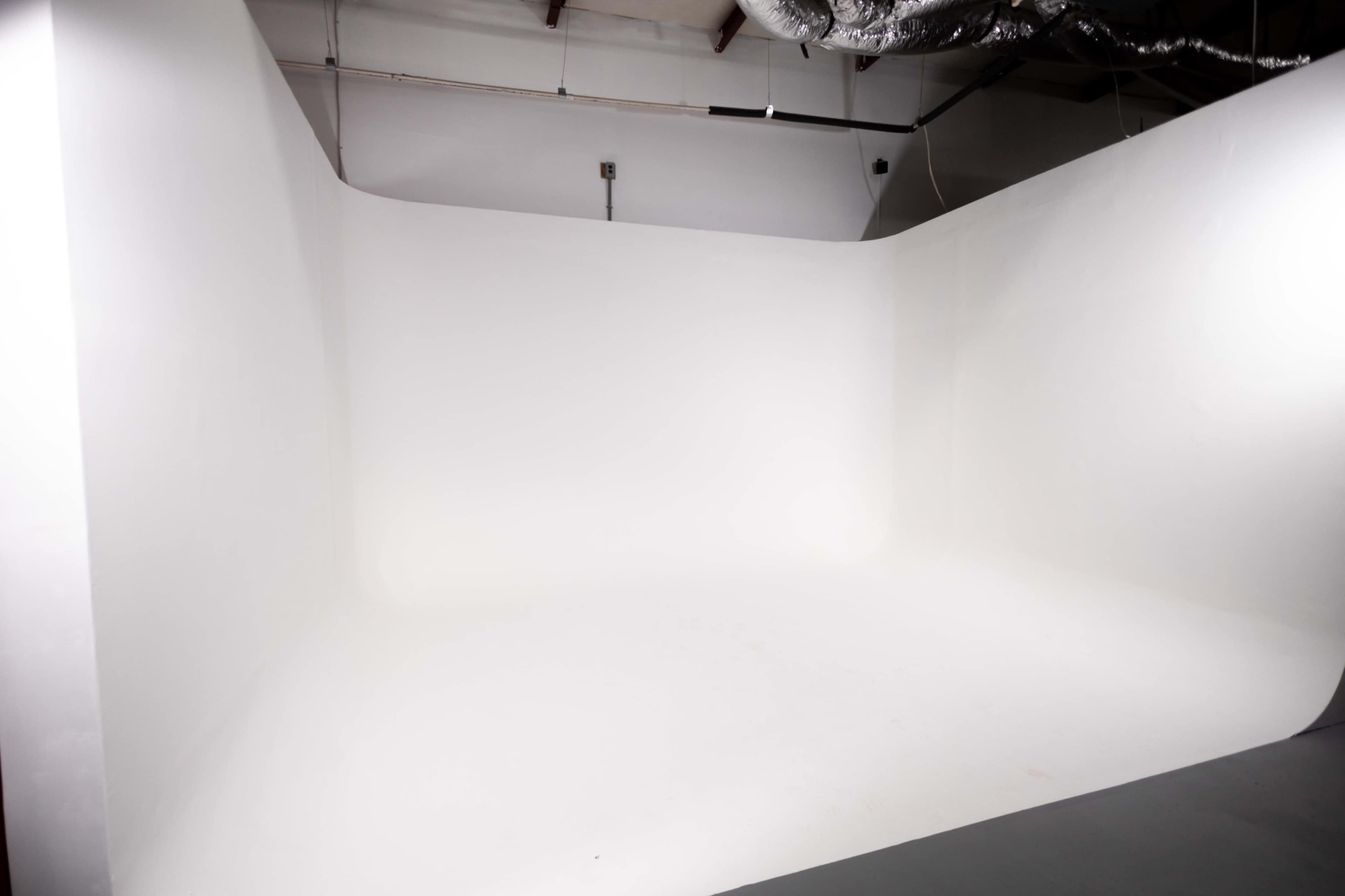 A spacious white photography studio with a seamless backdrop and polished floor.