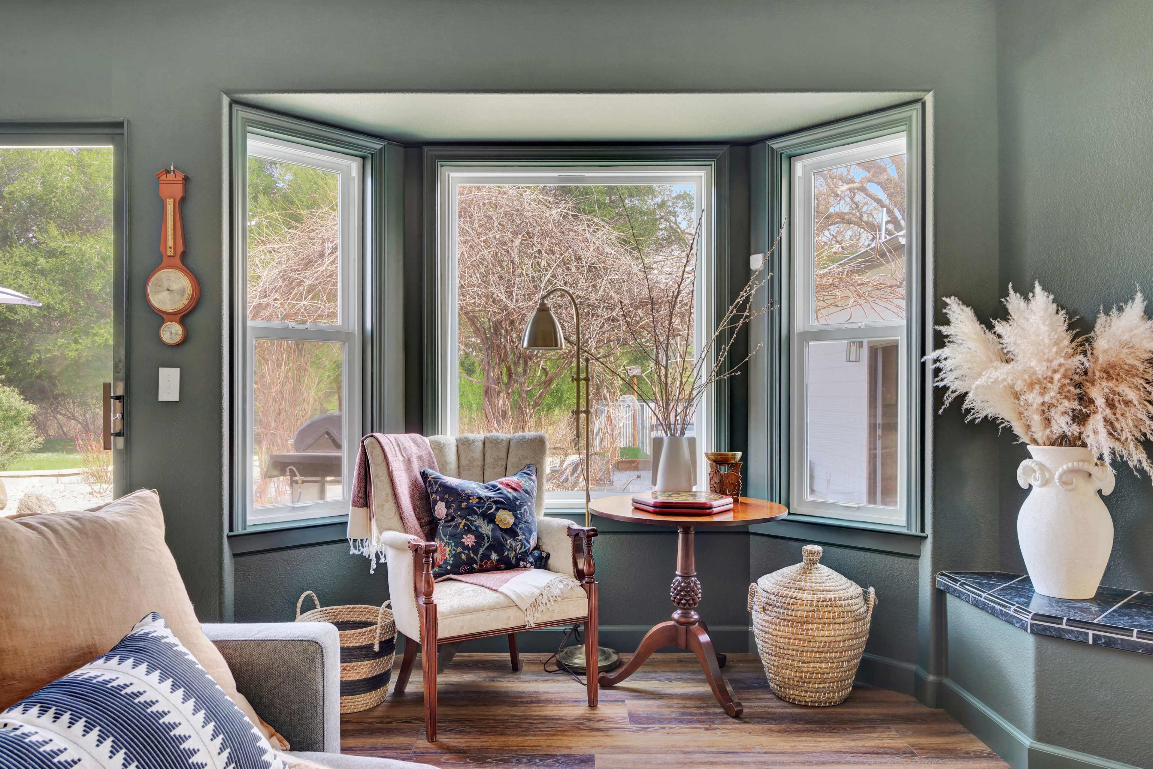 A cozy corner features a chair, a small table, and decorative items in a room with large windows overlooking an outdoor view.