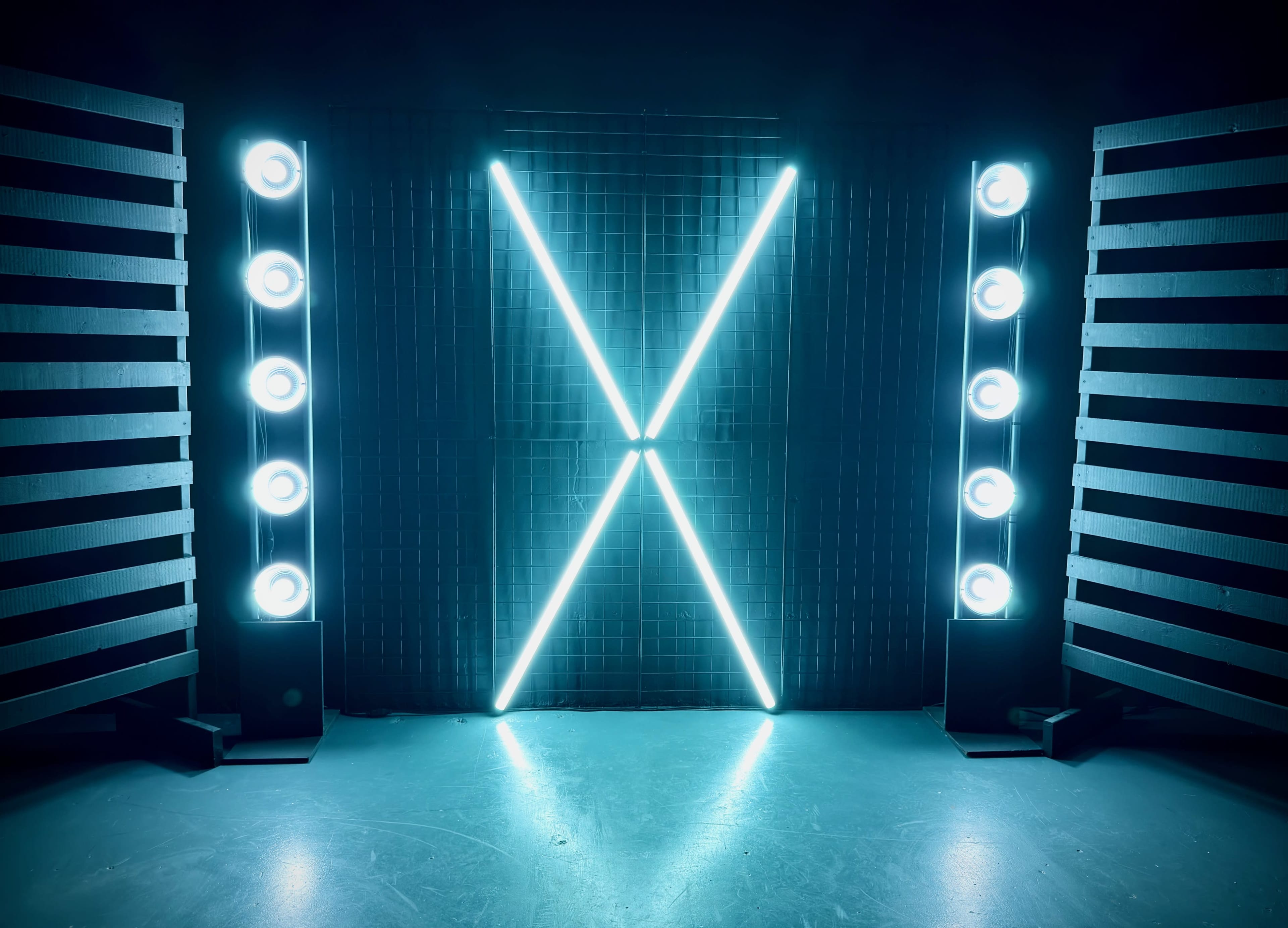 The image features two vertical light fixtures on either side of a grid backdrop, creating a large illuminated "X" in the center.