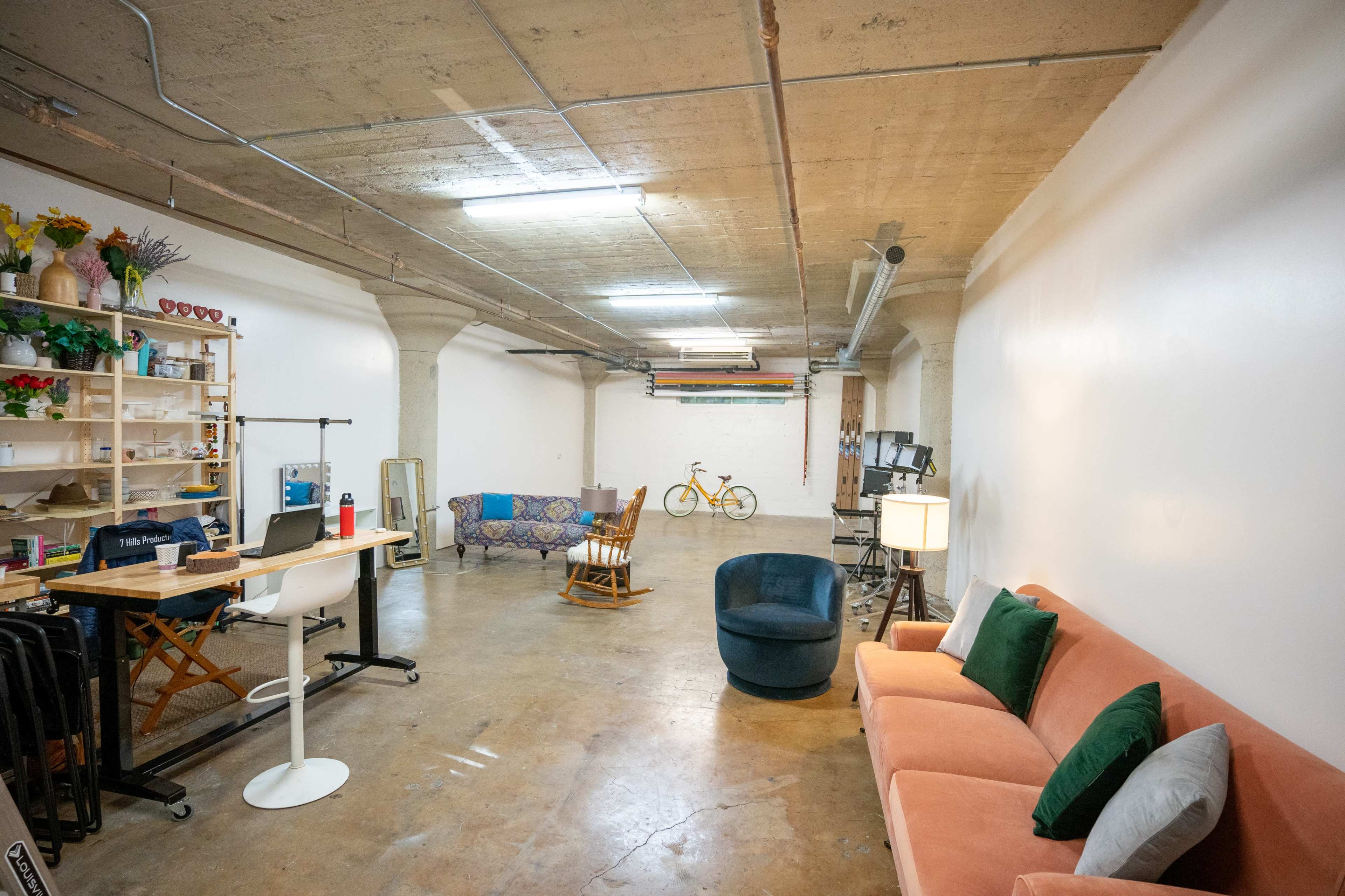 A spacious, well-lit room with a combination of seating areas, a desk workspace, and a bicycle in the background.
