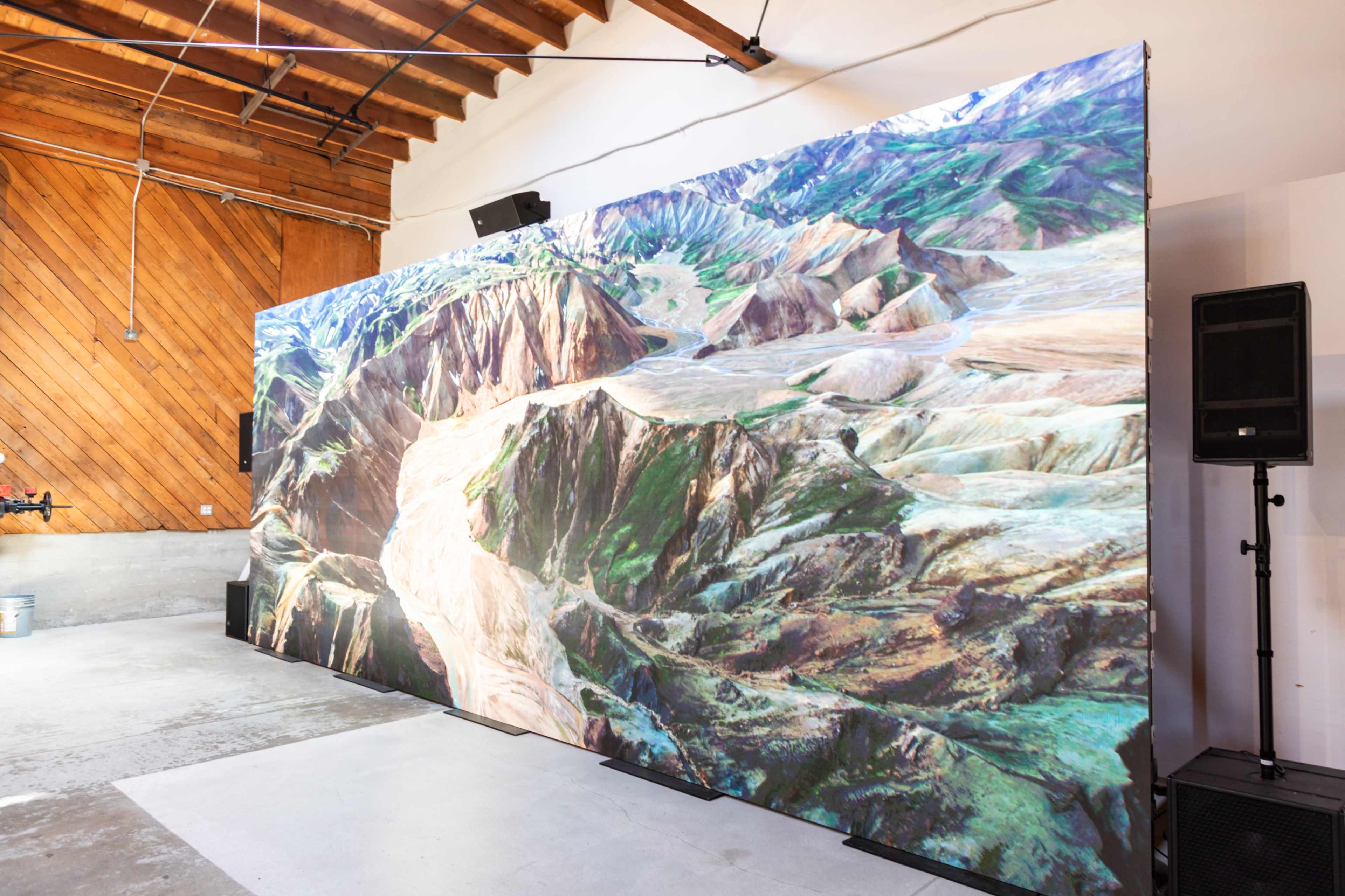 A large mural depicting a mountainous landscape is displayed on a wall in a room with wooden beams.
