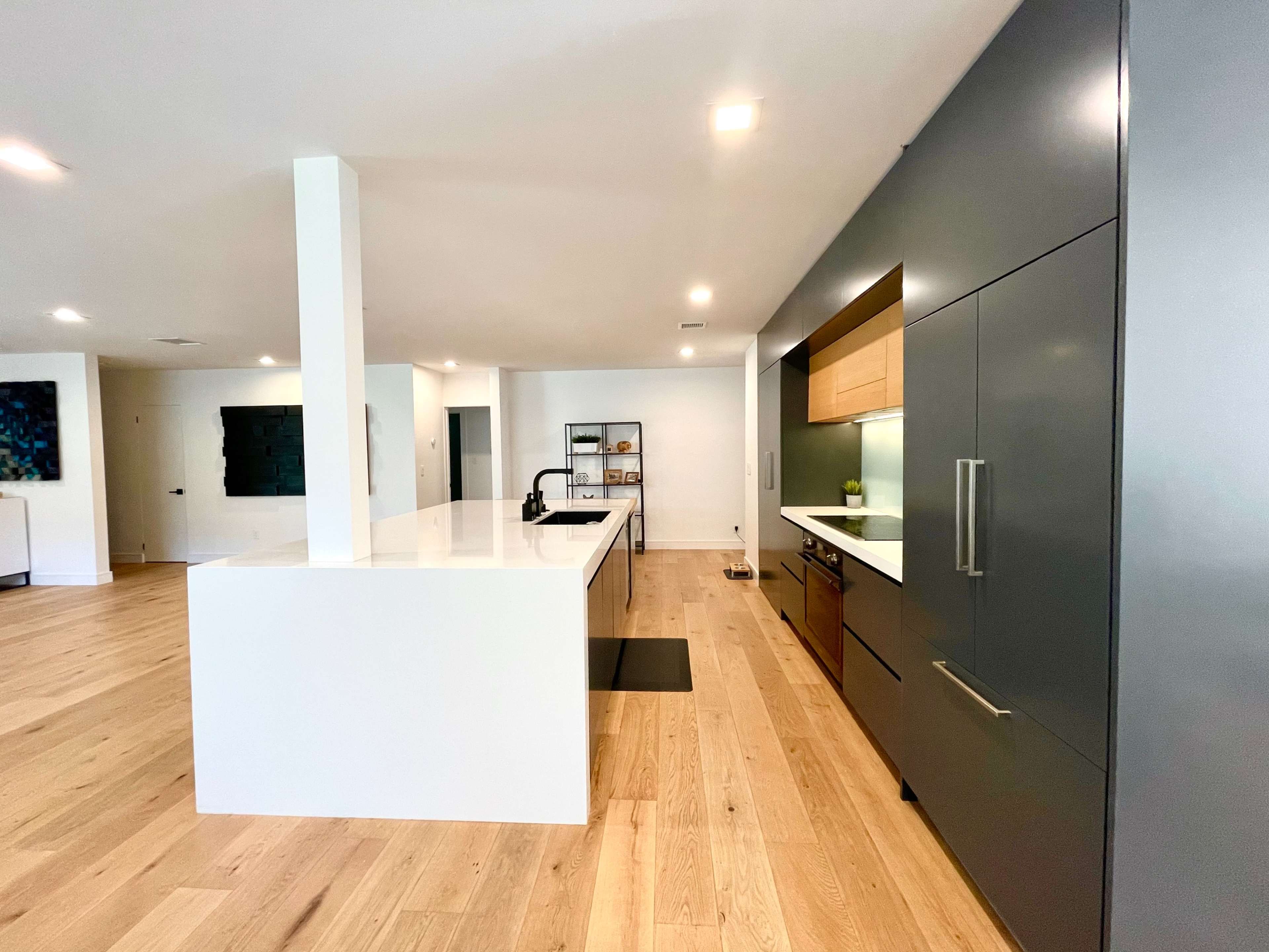 A modern kitchen with a large island, white countertops, dark cabinetry, and wooden flooring.