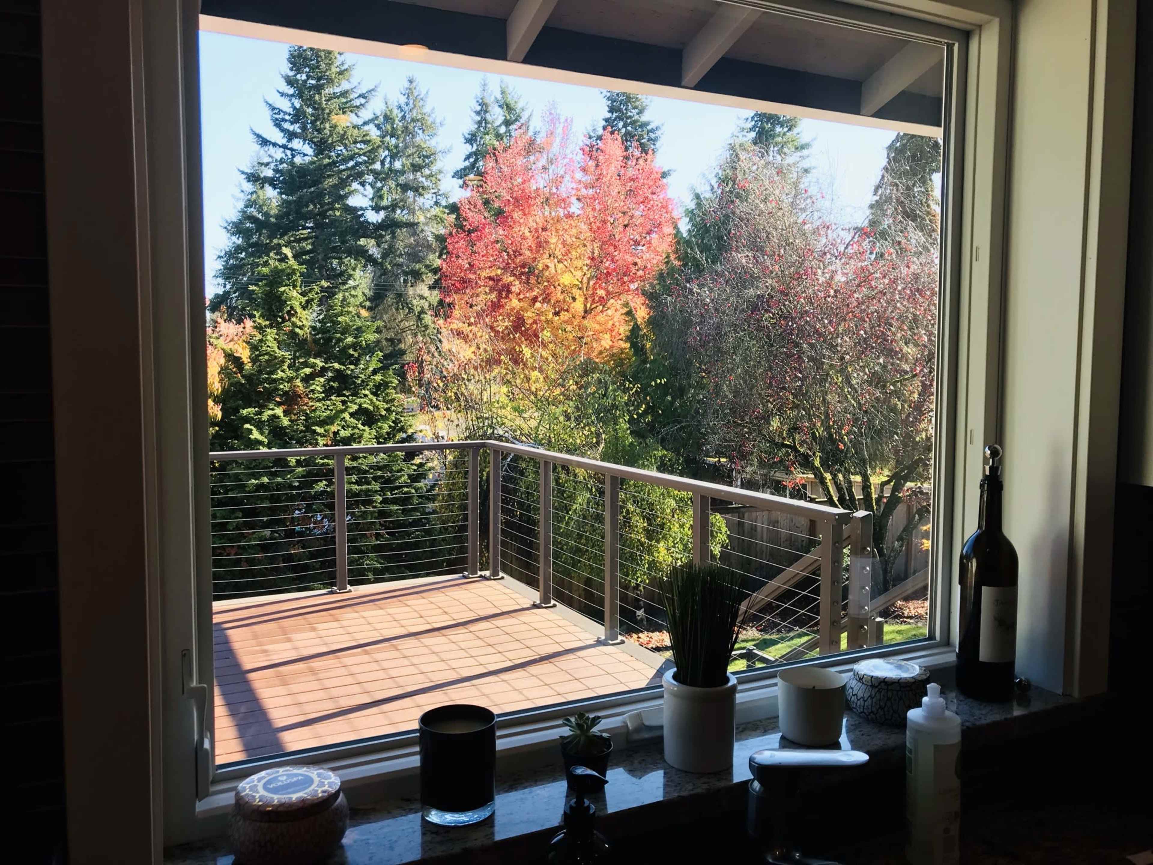 A window frames a view of a wooden deck surrounded by trees with autumn foliage.