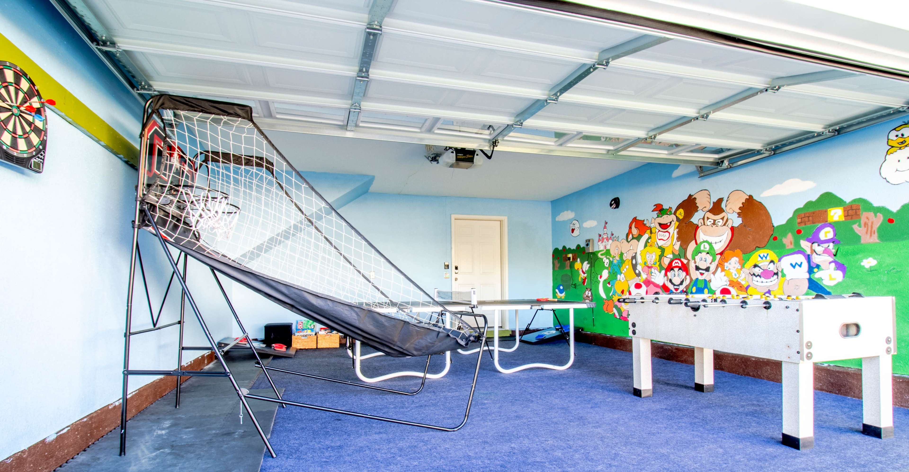 A garage with a basketball shooting game, a foosball table, and colorful cartoon characters painted on the wall.