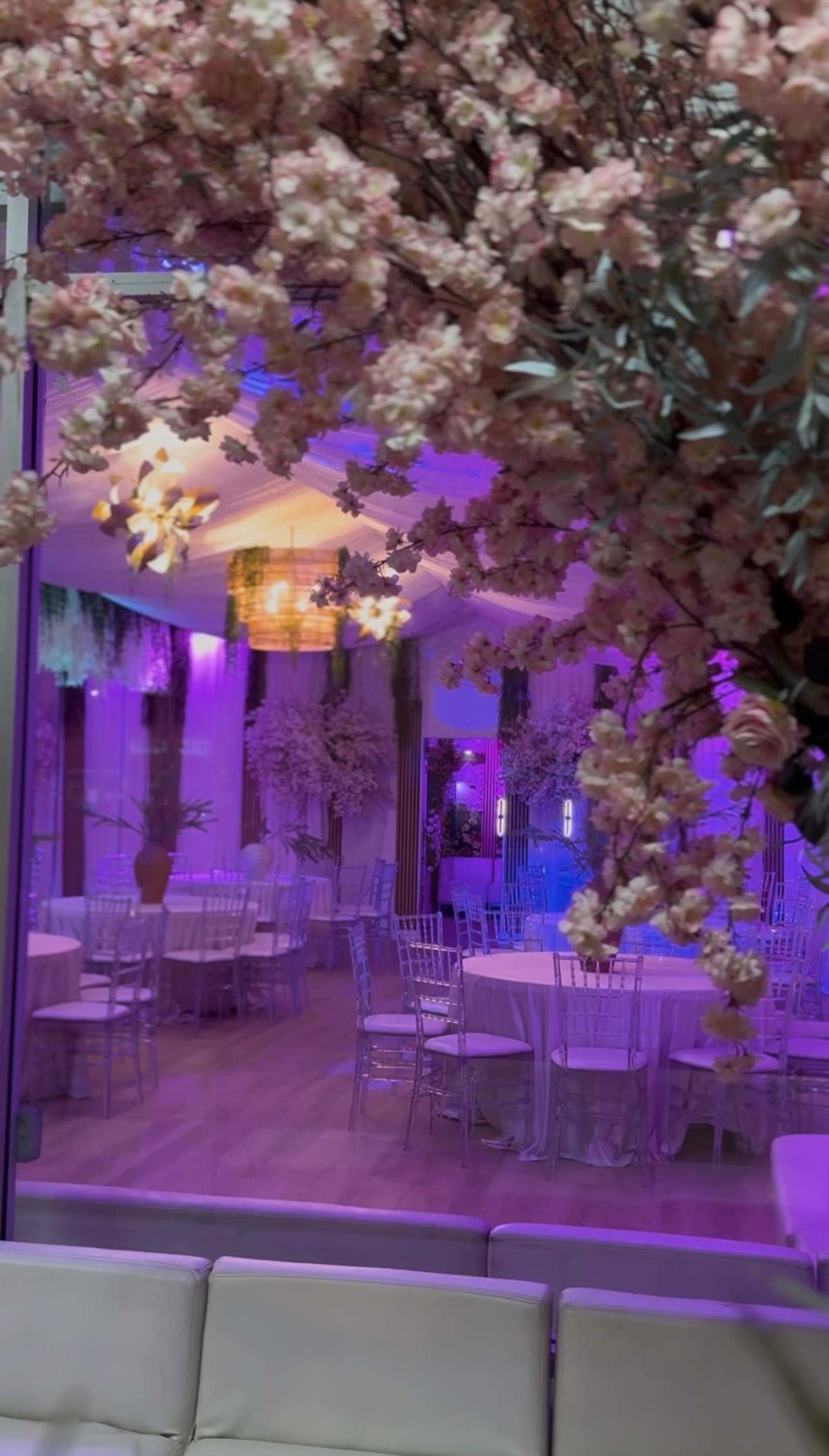 The image shows an upscale event space decorated with pink floral arrangements and illuminated in various shades of purple.