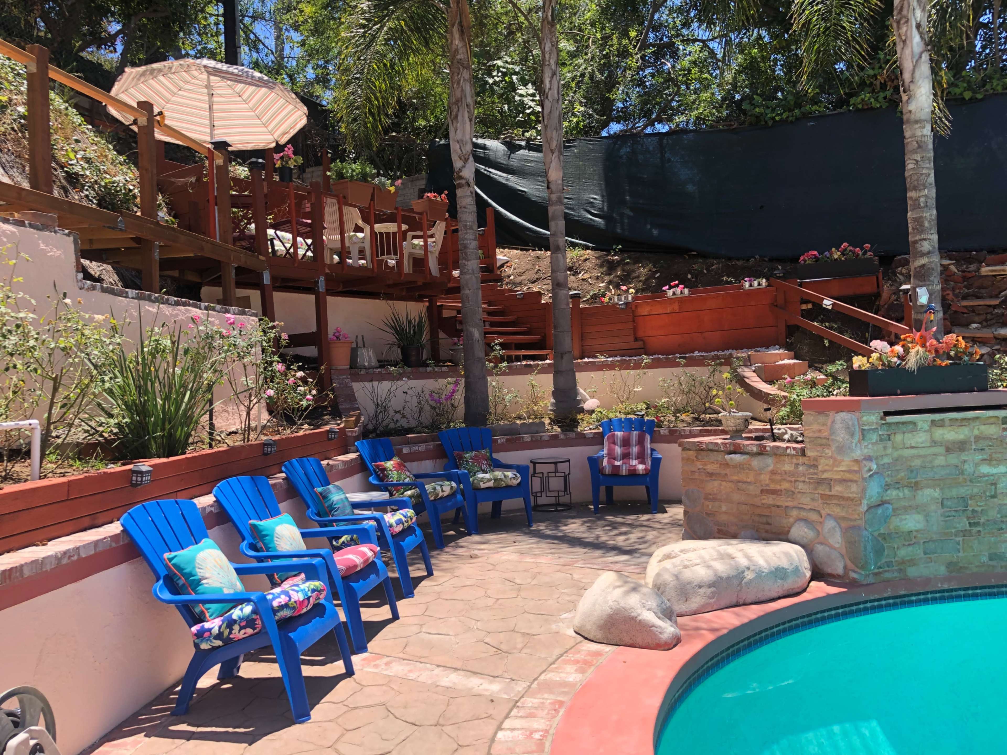 A landscaped backyard with a swimming pool, lounge chairs, and tiered wooden decking surrounded by greenery.