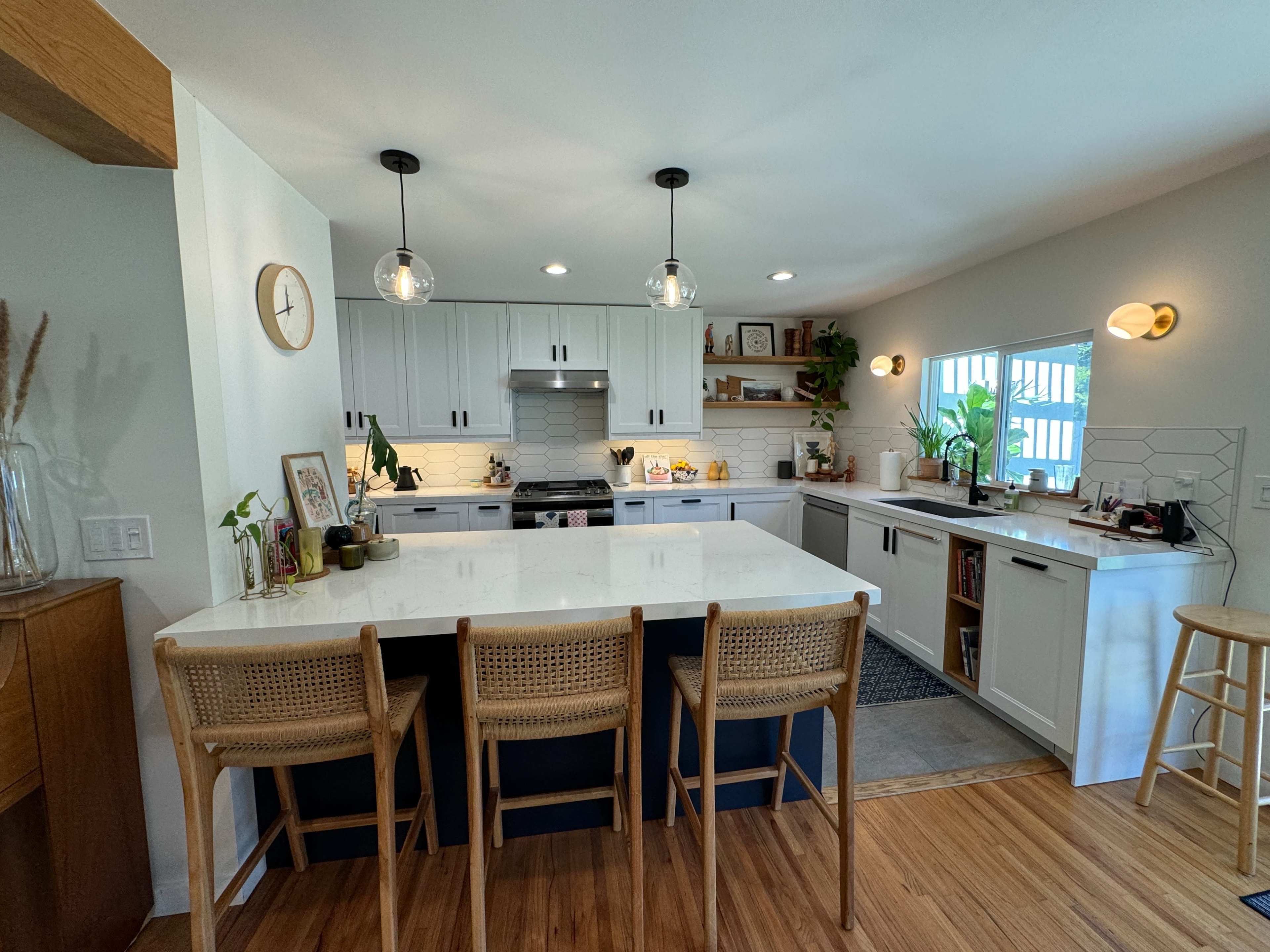 A modern kitchen features white cabinets, a large island with bar stools, and natural light streaming in from a window.