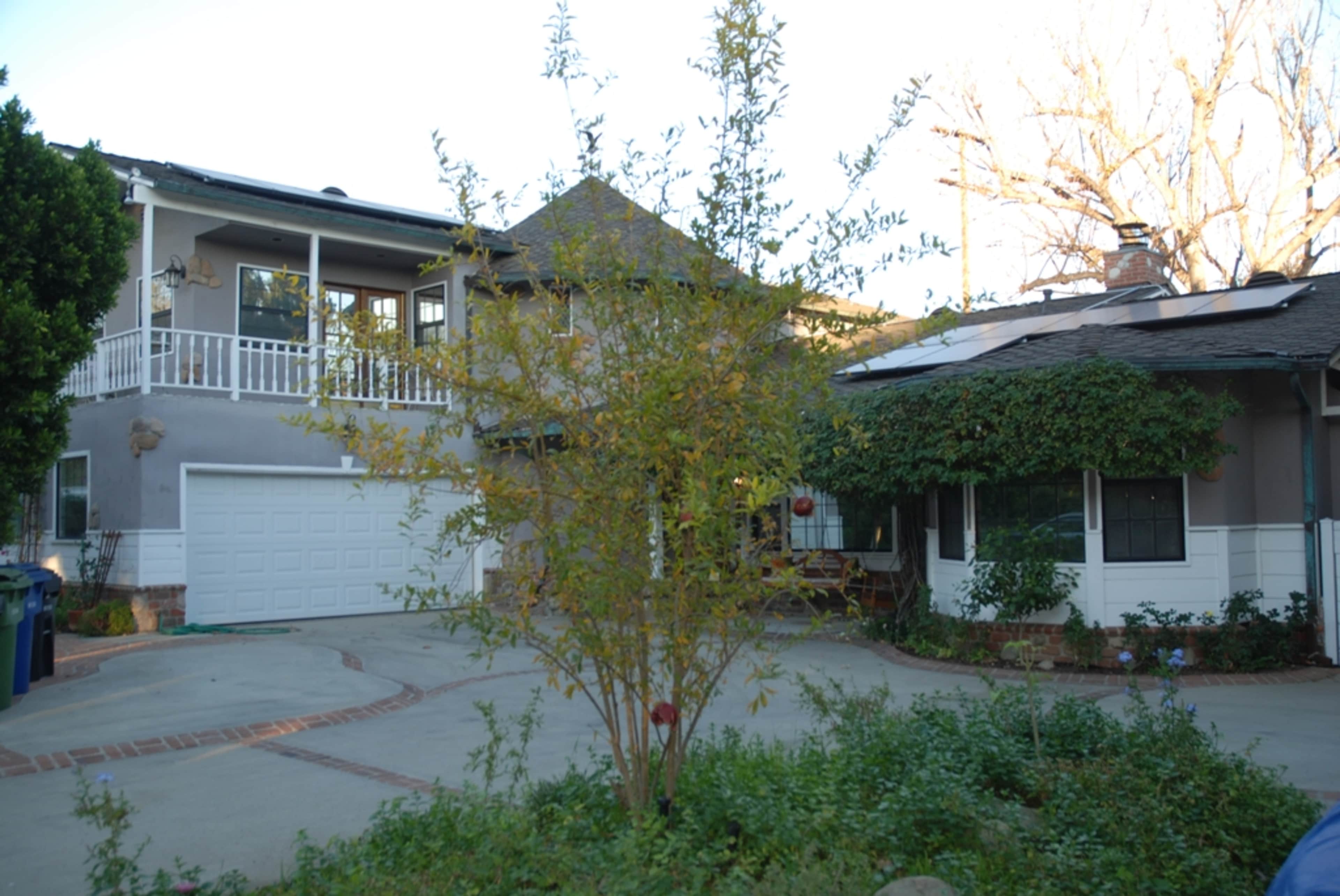 A two-story house with a garage and a front porch is surrounded by a landscaped driveway and small trees.