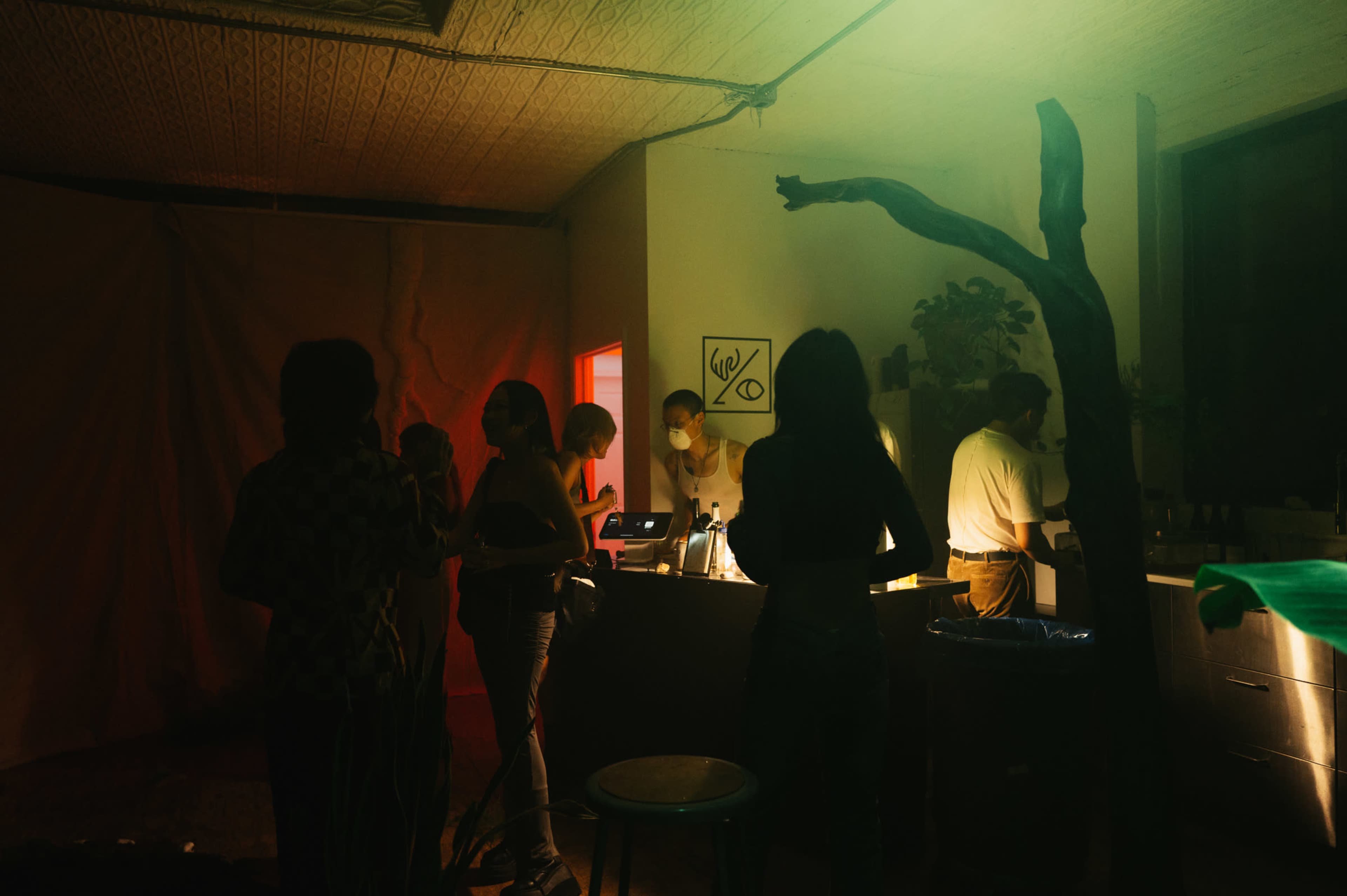 A dimly lit room with people gathered around a bar while others engage in conversation.