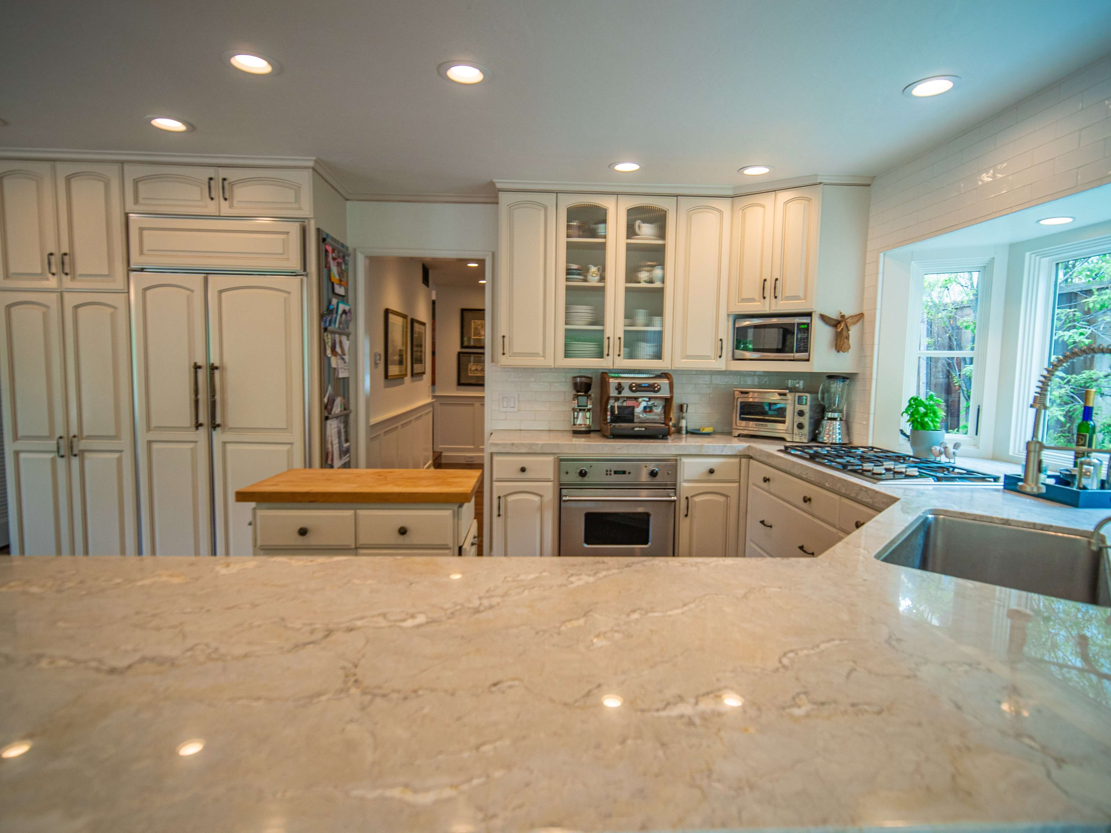 The kitchen features white cabinetry, a central wooden island, and modern appliances arranged around a light marble countertop.