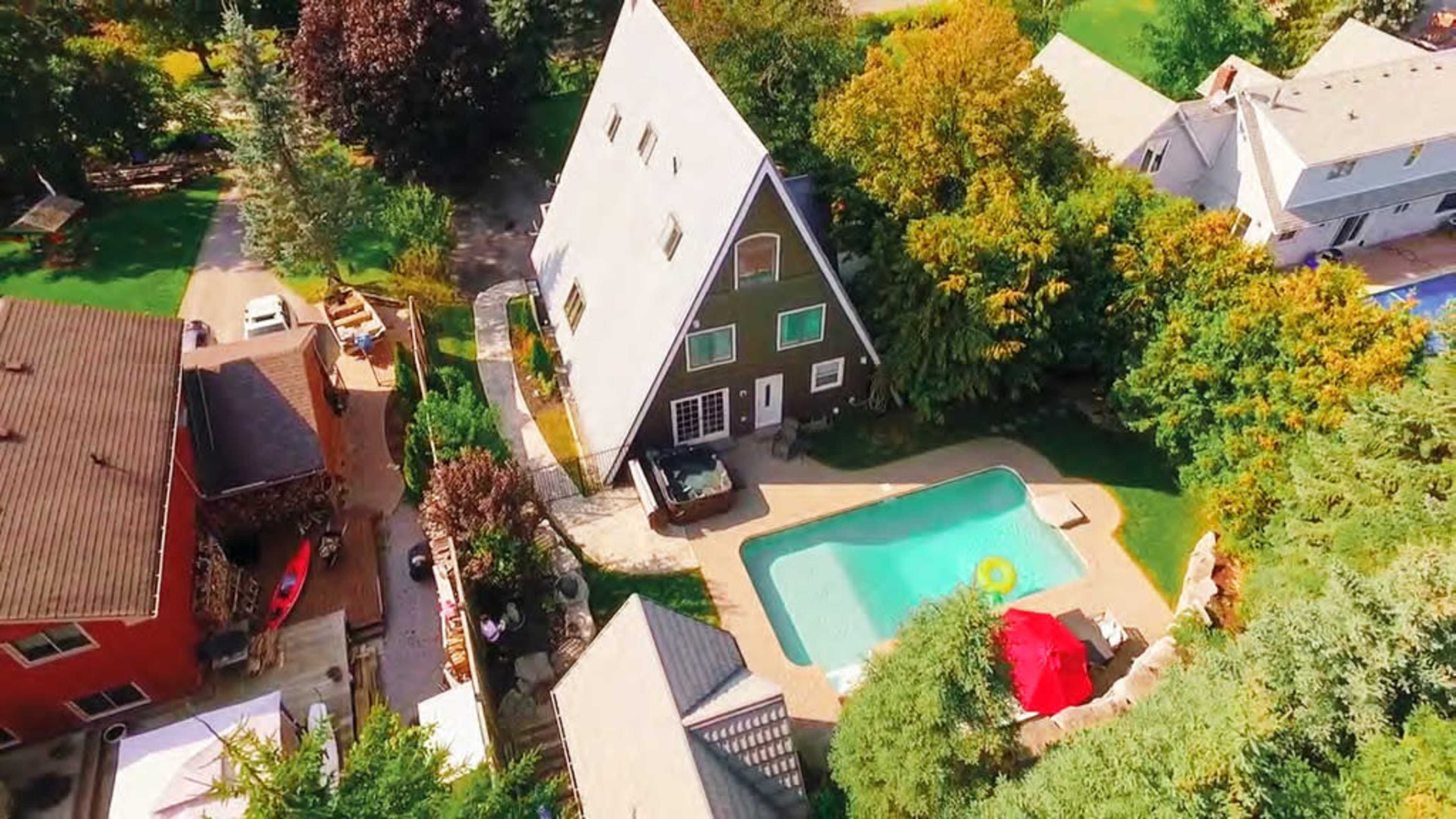 An aerial view of a property featuring a large A-frame house, a swimming pool, and surrounding greenery.