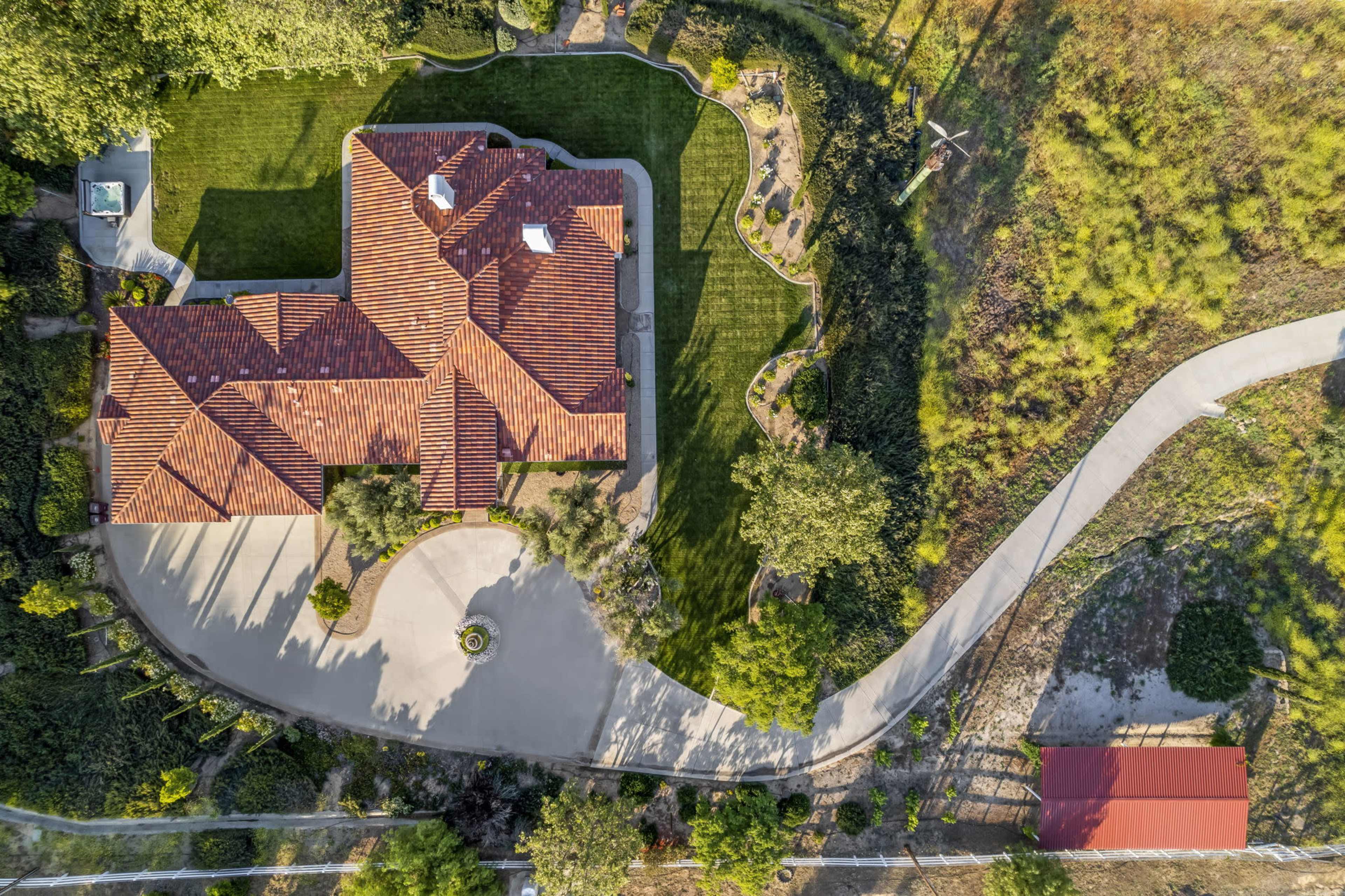 An aerial view of a large residential property featuring a house with a red tiled roof, manicured lawns, and a winding driveway.