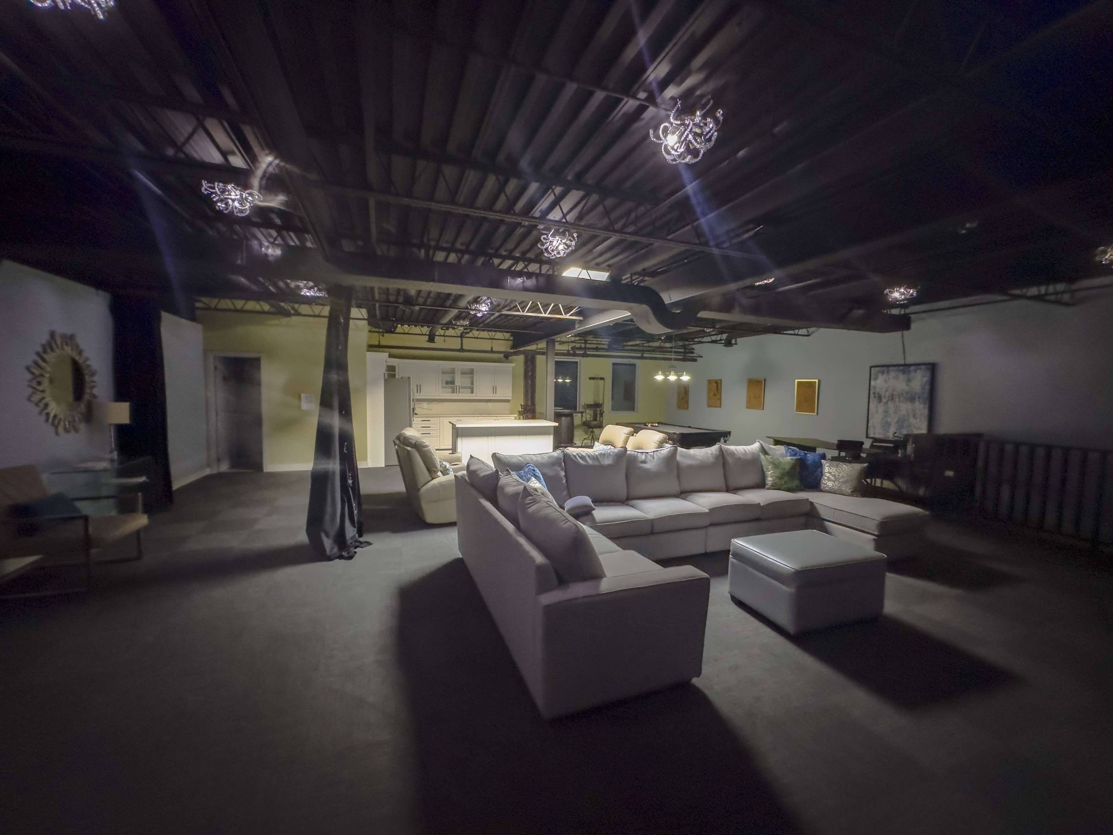 A spacious lounge area features a large, L-shaped sectional sofa and a coffee table, with various seating and artwork along the walls.