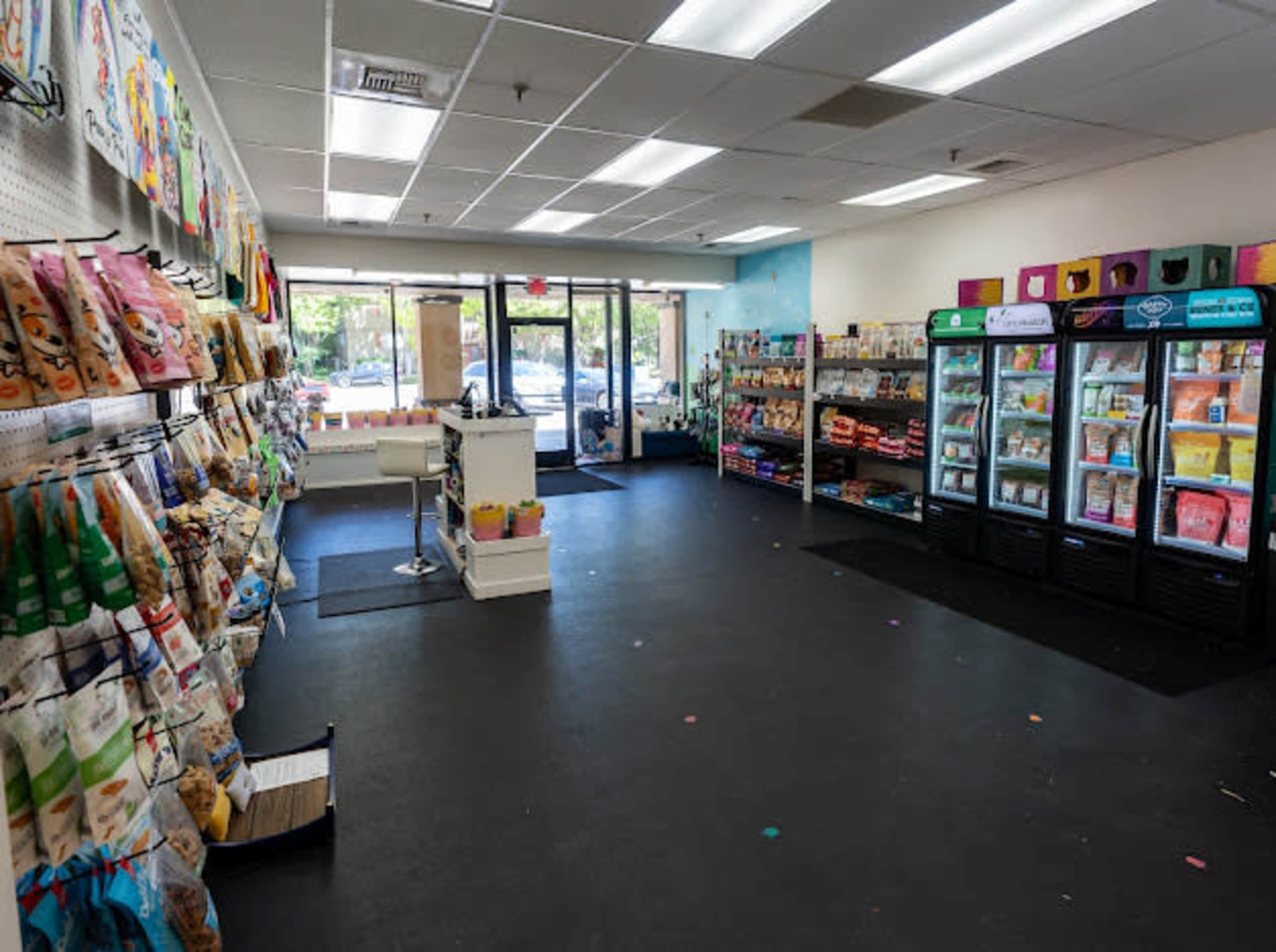 The image shows the interior of a pet supply store with shelves lined with pet food and products on one side, and a refrigeration unit displaying pet items on the opposite side.