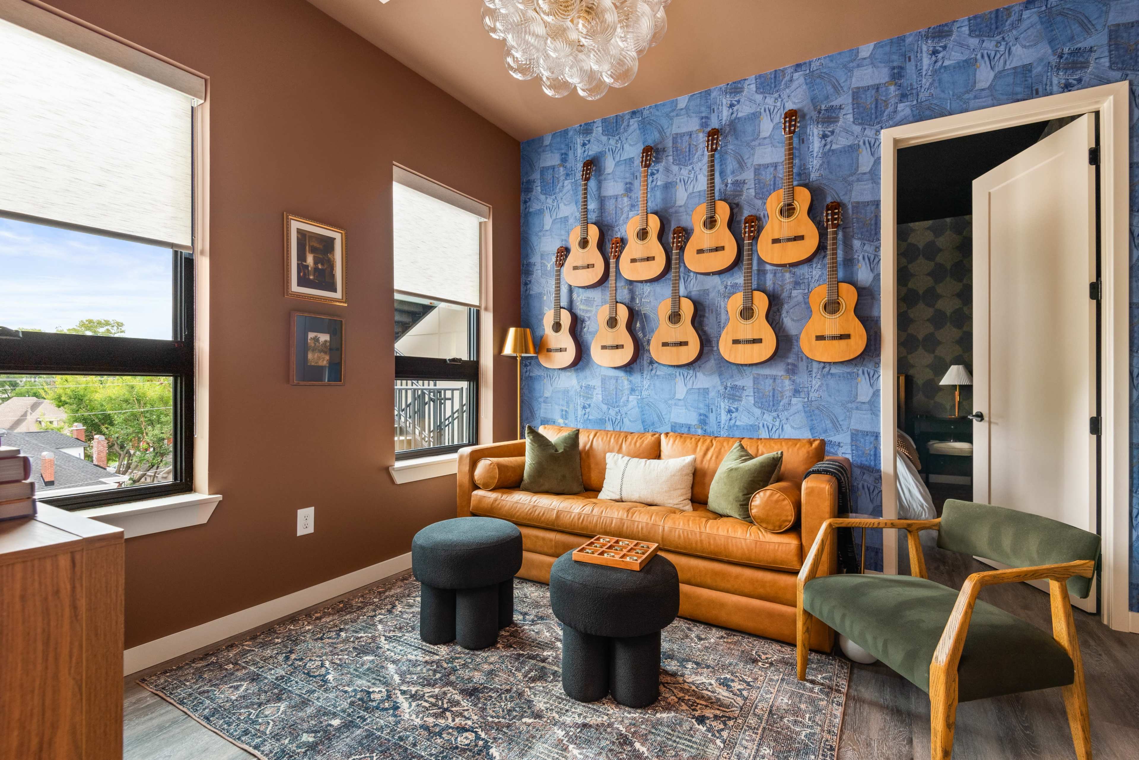 The image features a cozy room with a brown wall, a blue accent wall adorned with guitars, a leather sofa, two small black stools, and a green armchair.
