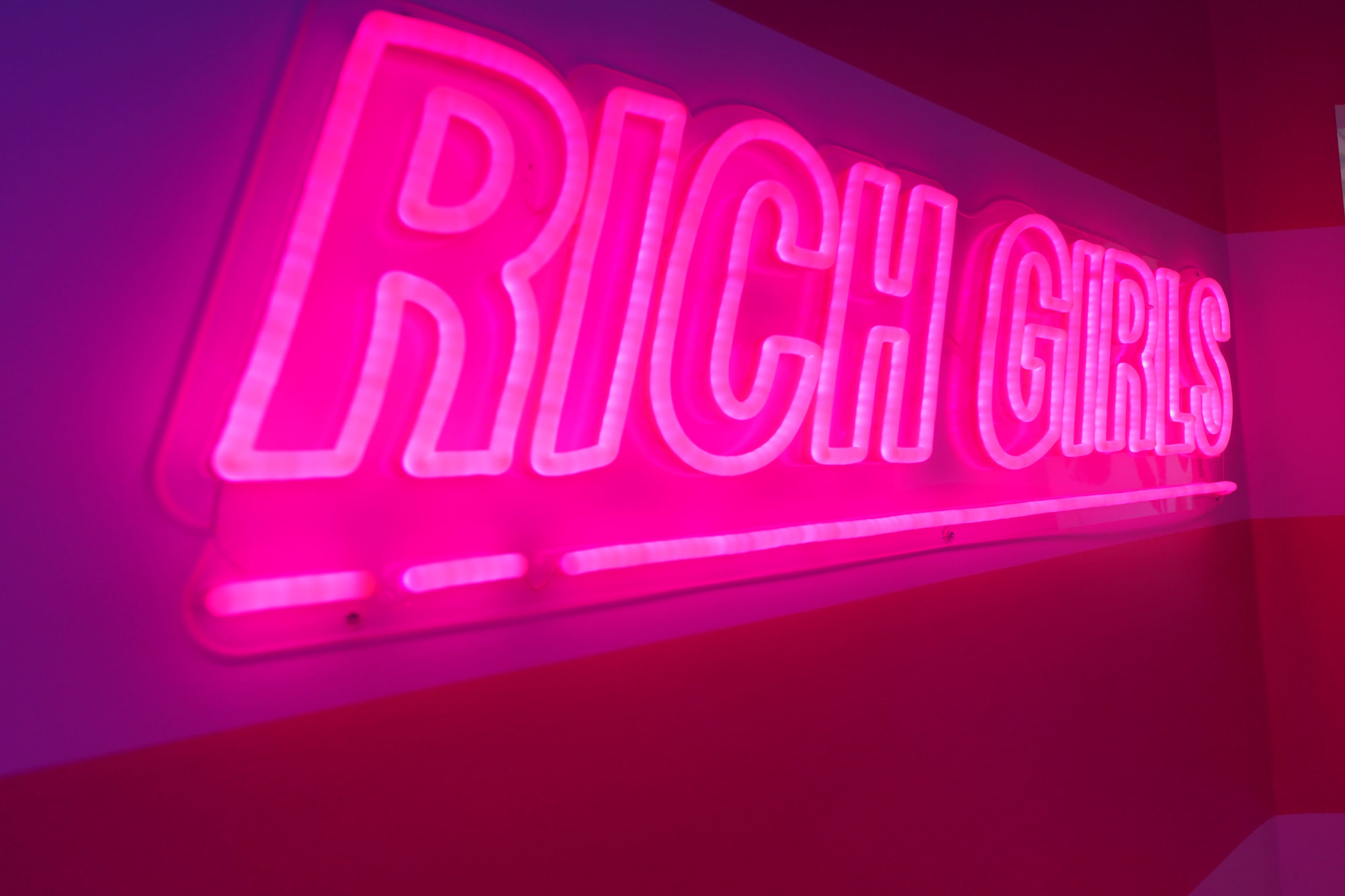 A glowing pink neon sign displays the words "RICH GIRLS" against a brightly colored background.