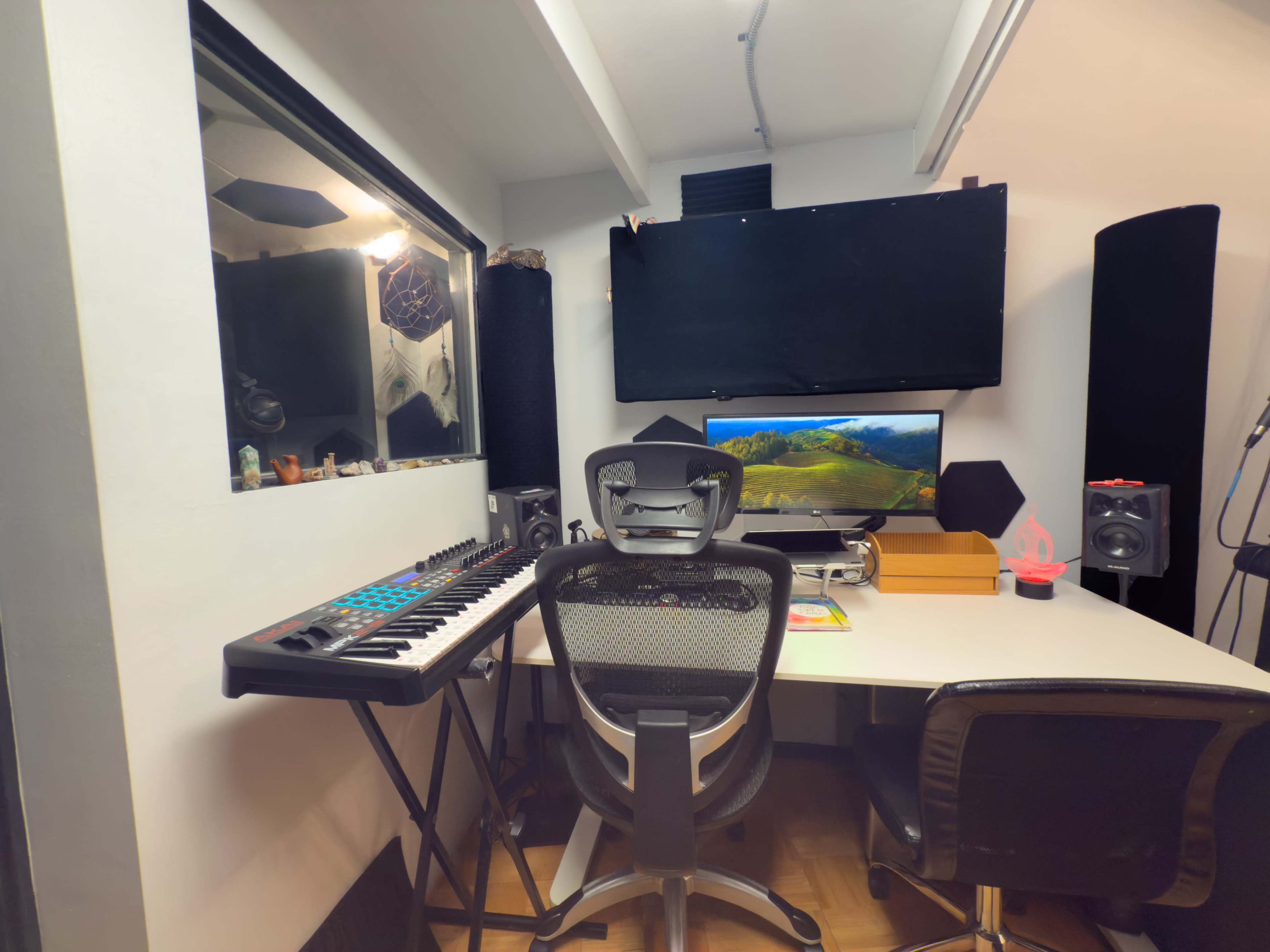 The image shows a modern music production studio with a keyboard, an ergonomic chair, and a computer setup on a white desk.