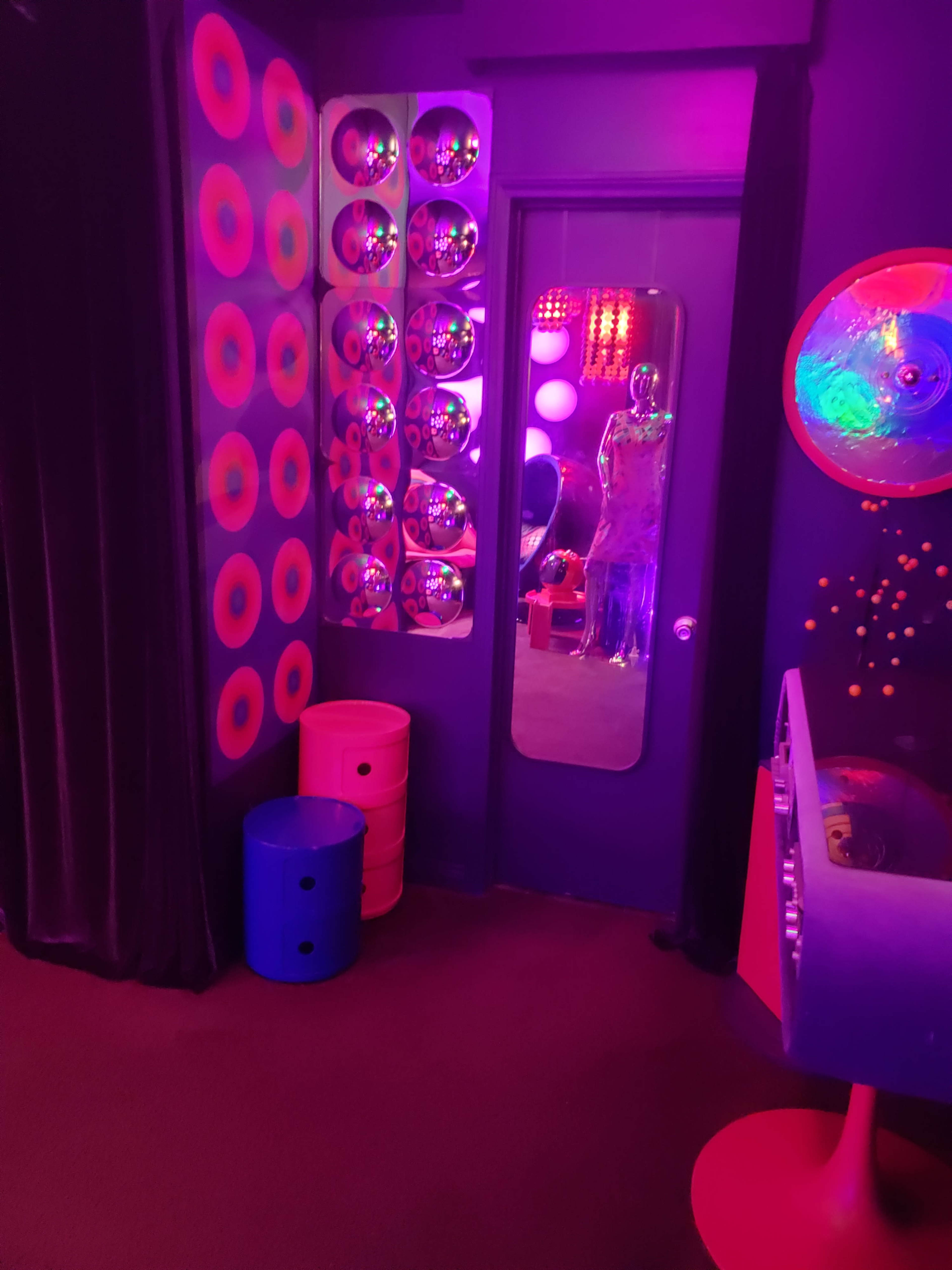A colorful room features a mirror, circular decor on the walls, and two brightly colored barrels.