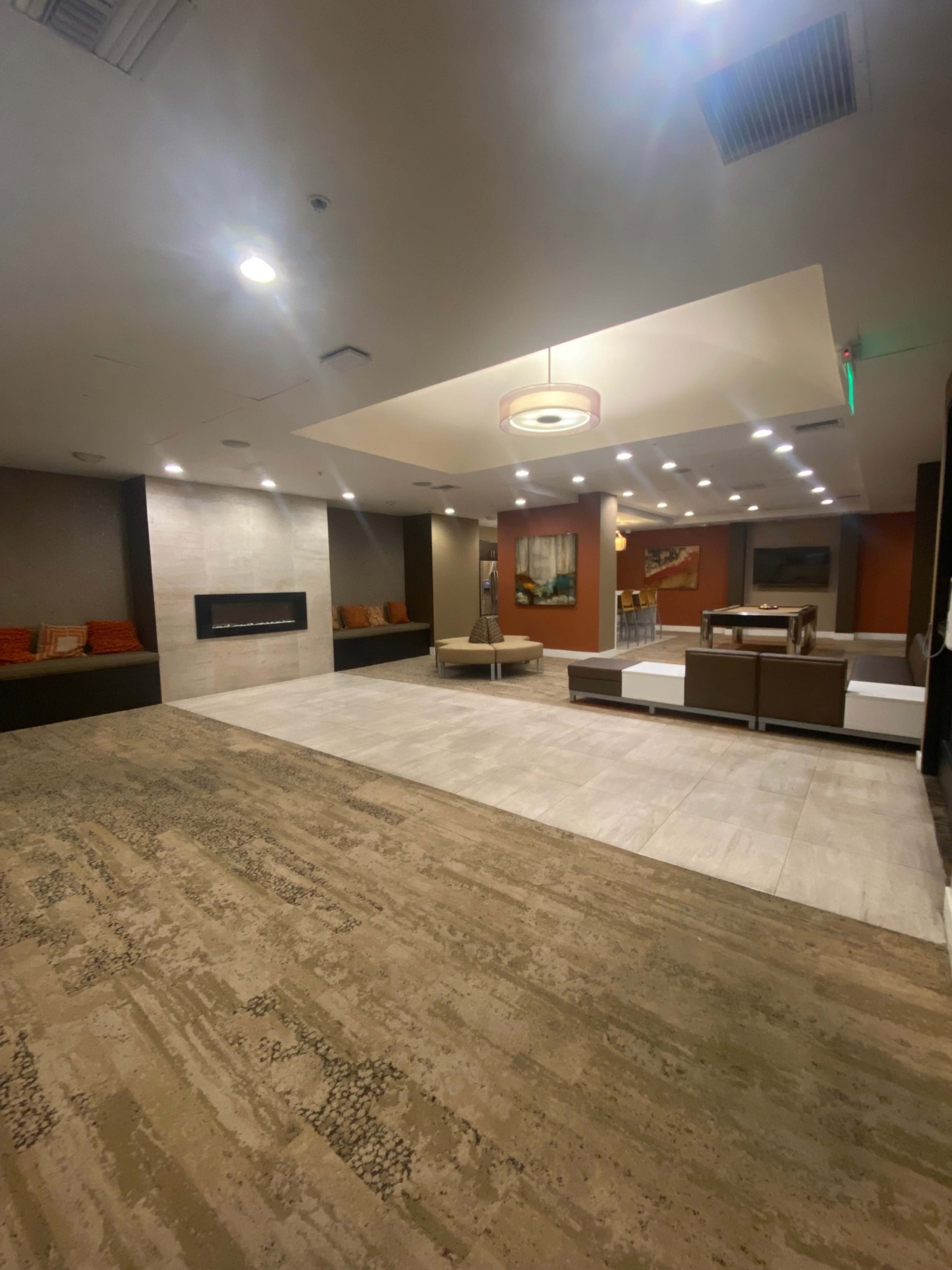 The image shows a spacious, modern lounge area featuring a fireplace, seating arrangements, and decorative artwork on the walls.