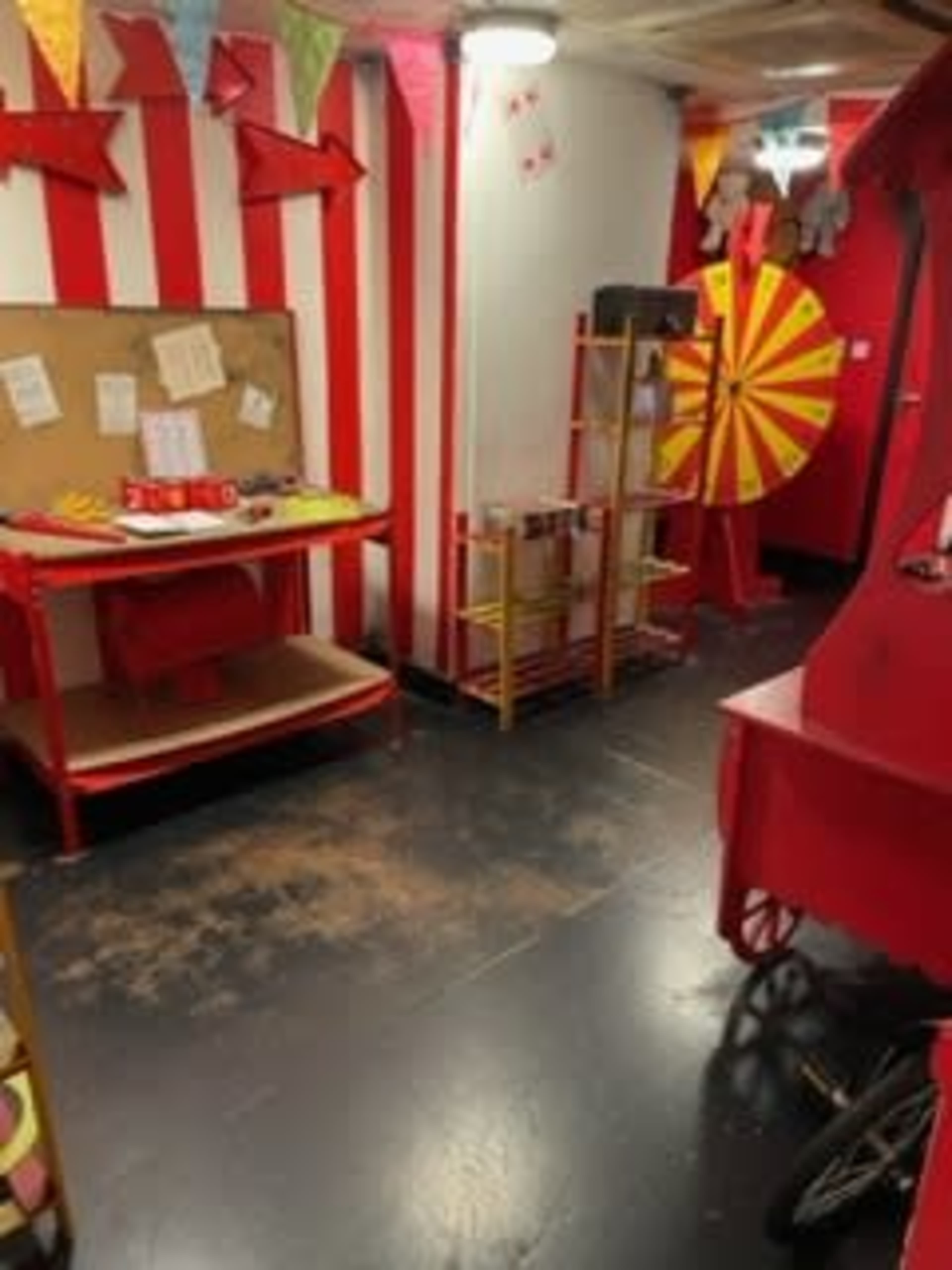 The scene shows a carnival-themed room with red and white striped walls, a bulletin board, a spinning prize wheel, and various festive decorations.
