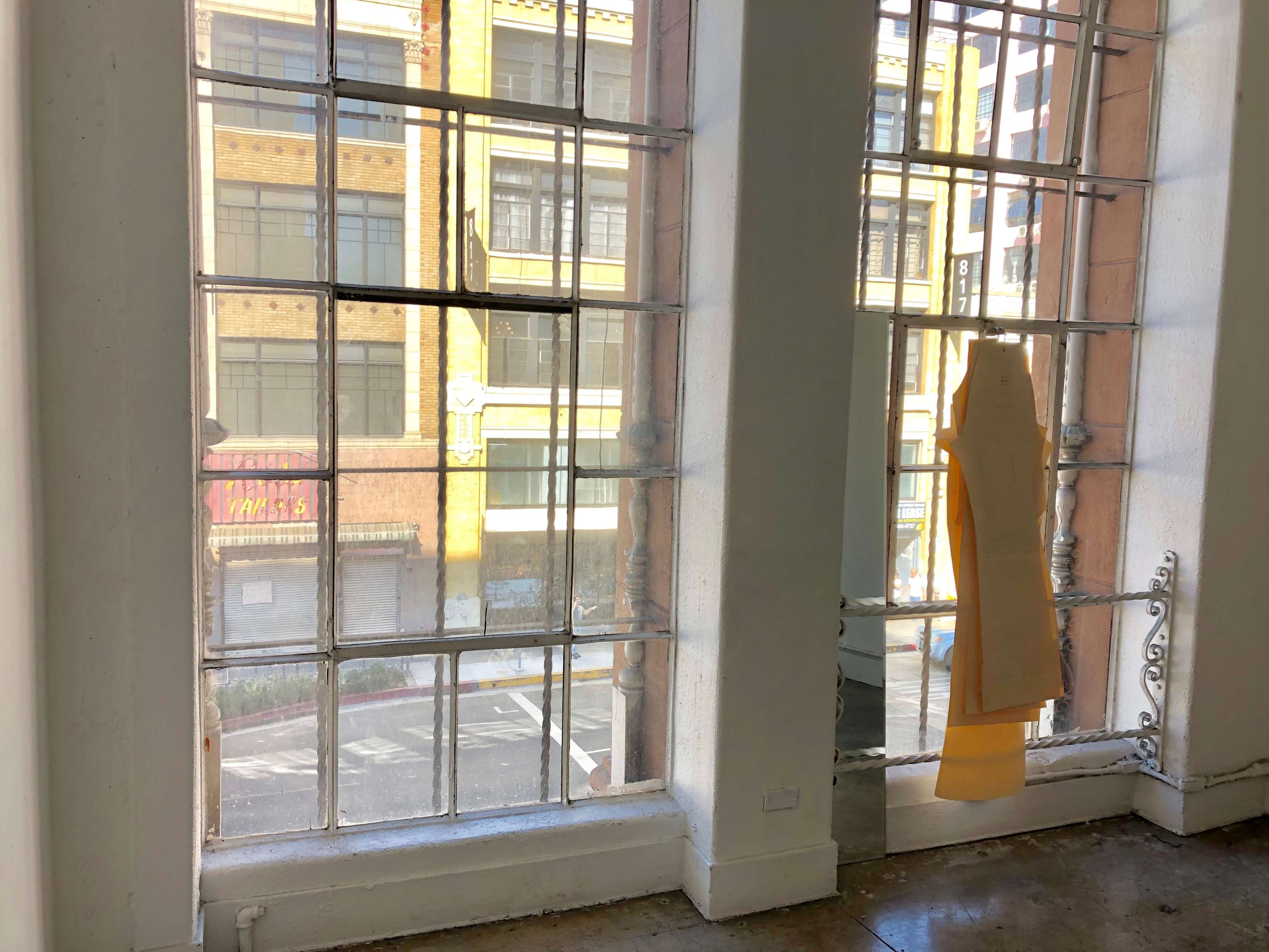 Large, grid-patterned windows overlooking a street with buildings across the way, and a piece of yellow fabric hanging on one window.