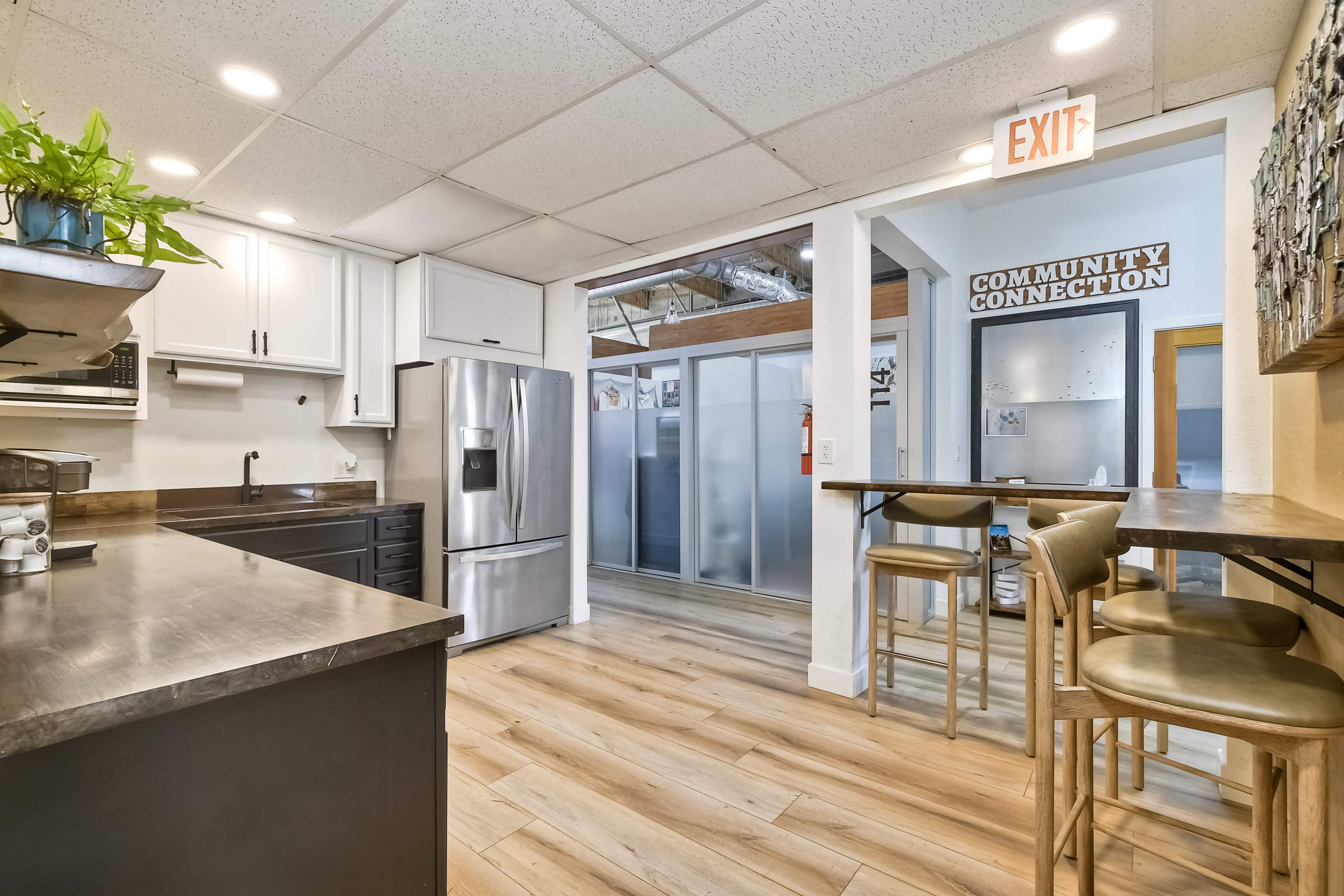 The image shows a modern kitchen with stainless steel appliances, wooden flooring, and a bar with high stools.