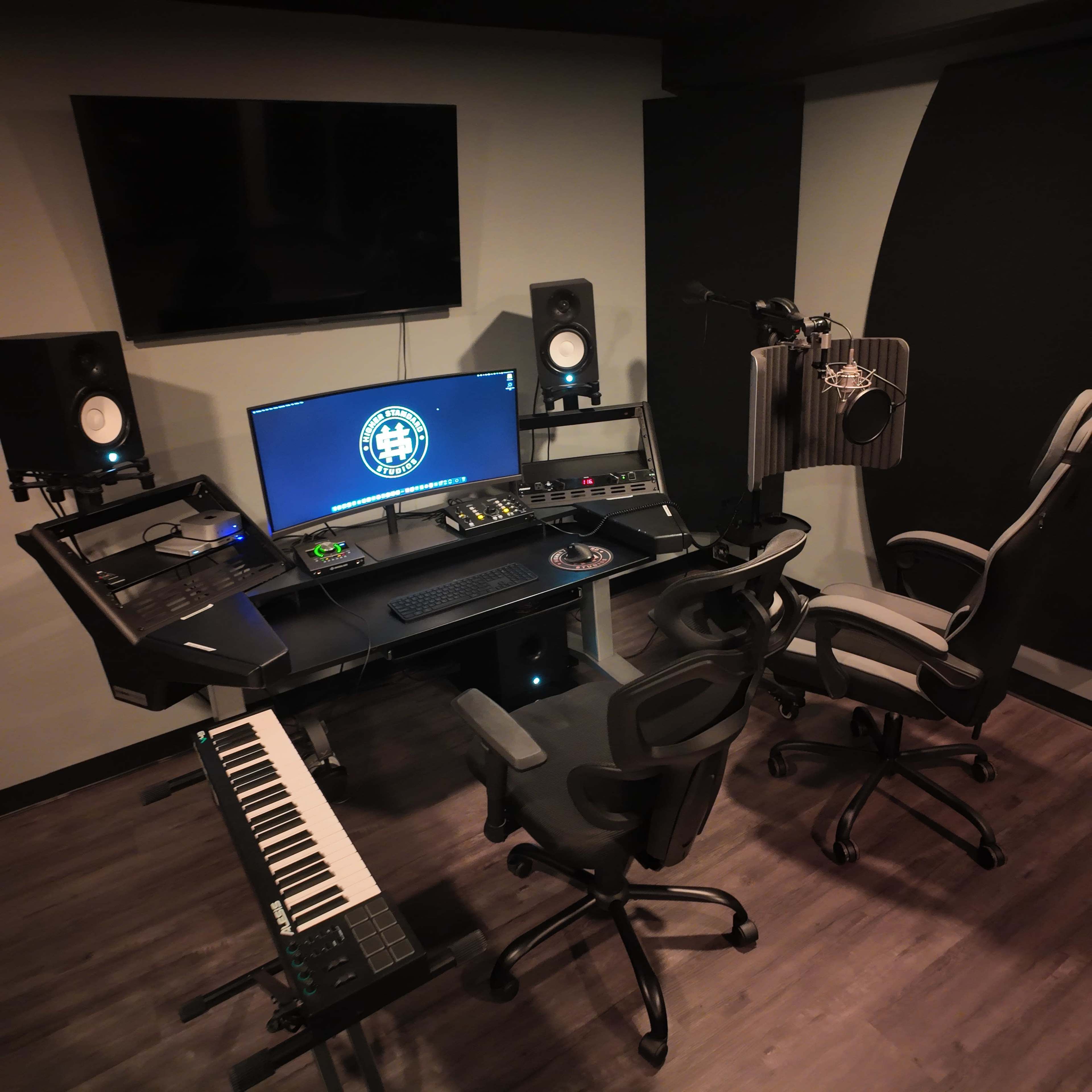 The image shows a modern recording studio setup with a computer workstation, audio monitors, a MIDI keyboard, and a microphone in a soundproof booth.