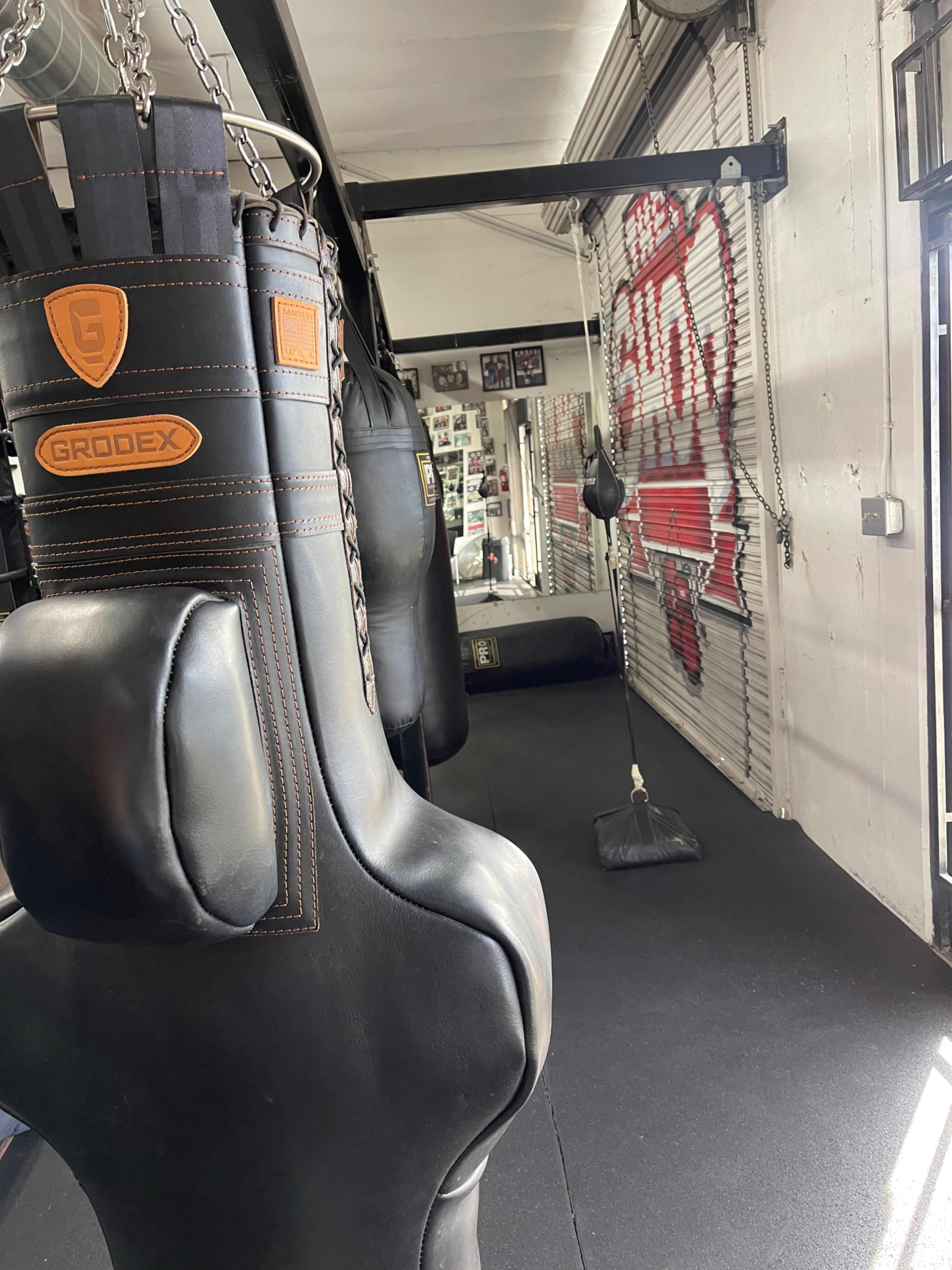 A fitness gym interior featuring several hanging punching bags and a padded floor.